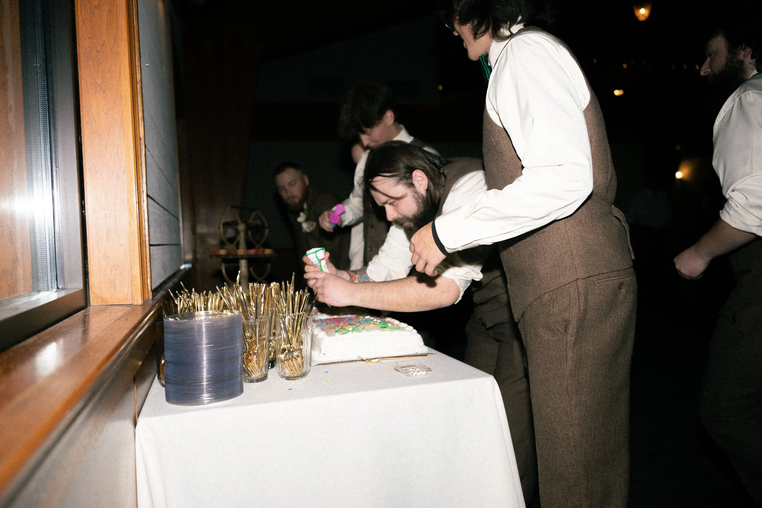 Group of people cutting a birthday cake with colorful icing and sprinkles at a celebration event.