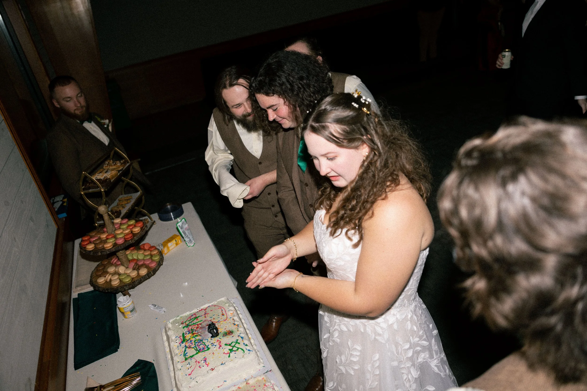 People gathered around a table with macarons, a cake with colorful sprinkles, and a small figurine, celebrating a special occasion.