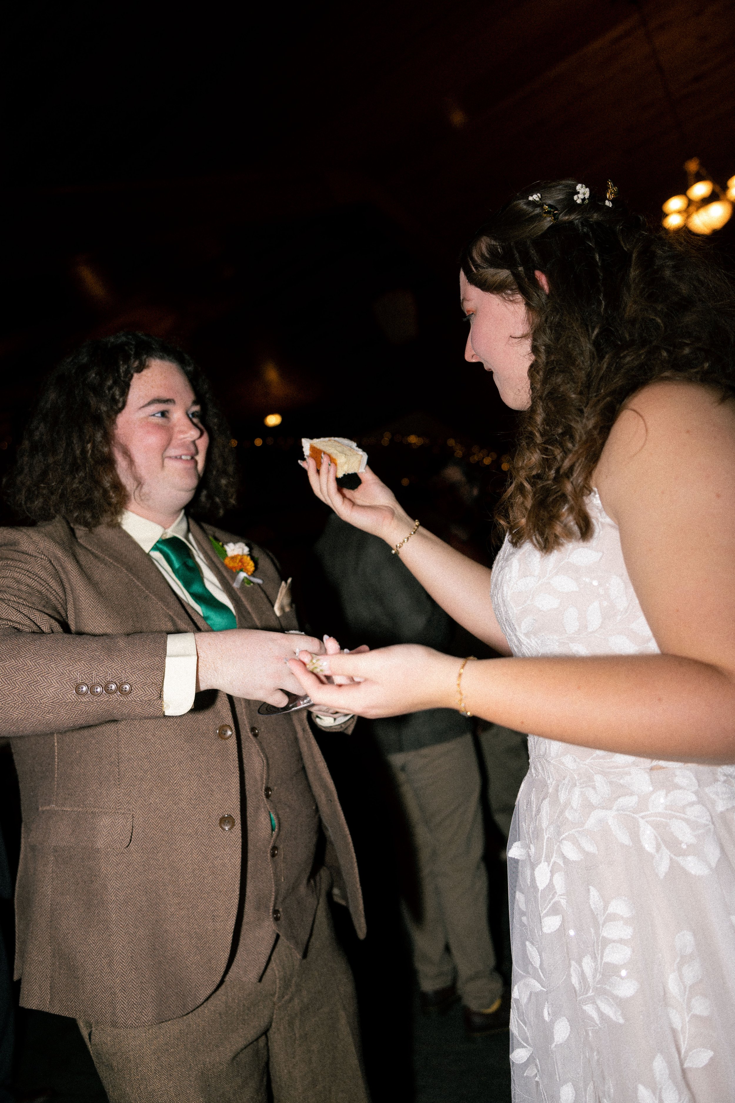 A same-sex couple exchanging rings during their wedding ceremony, with one person holding a small piece of cake.