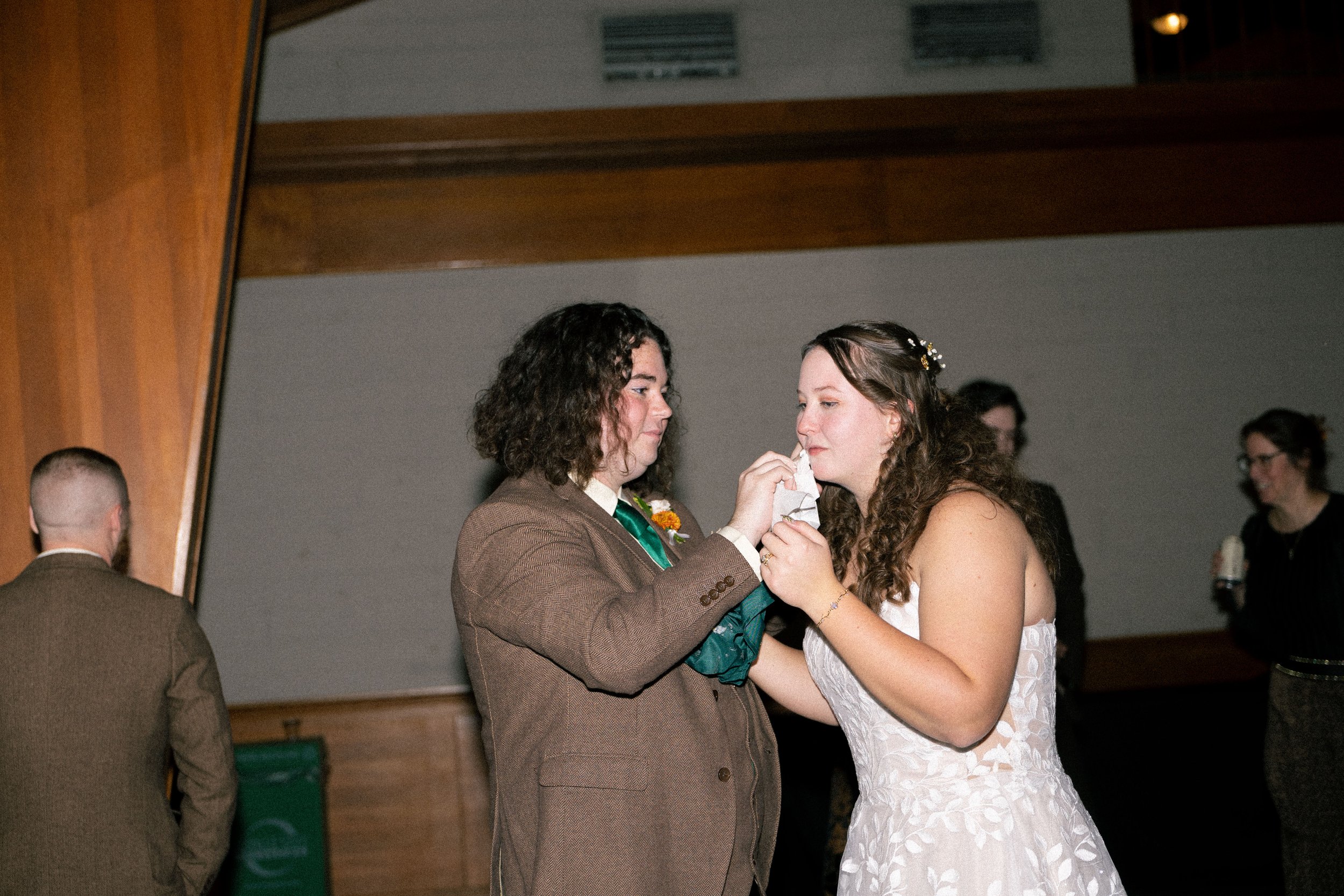 A couple, dressed in wedding attire, sharing a moment on the dance floor during a wedding celebration. The groom is feeding the bride a piece of cake.