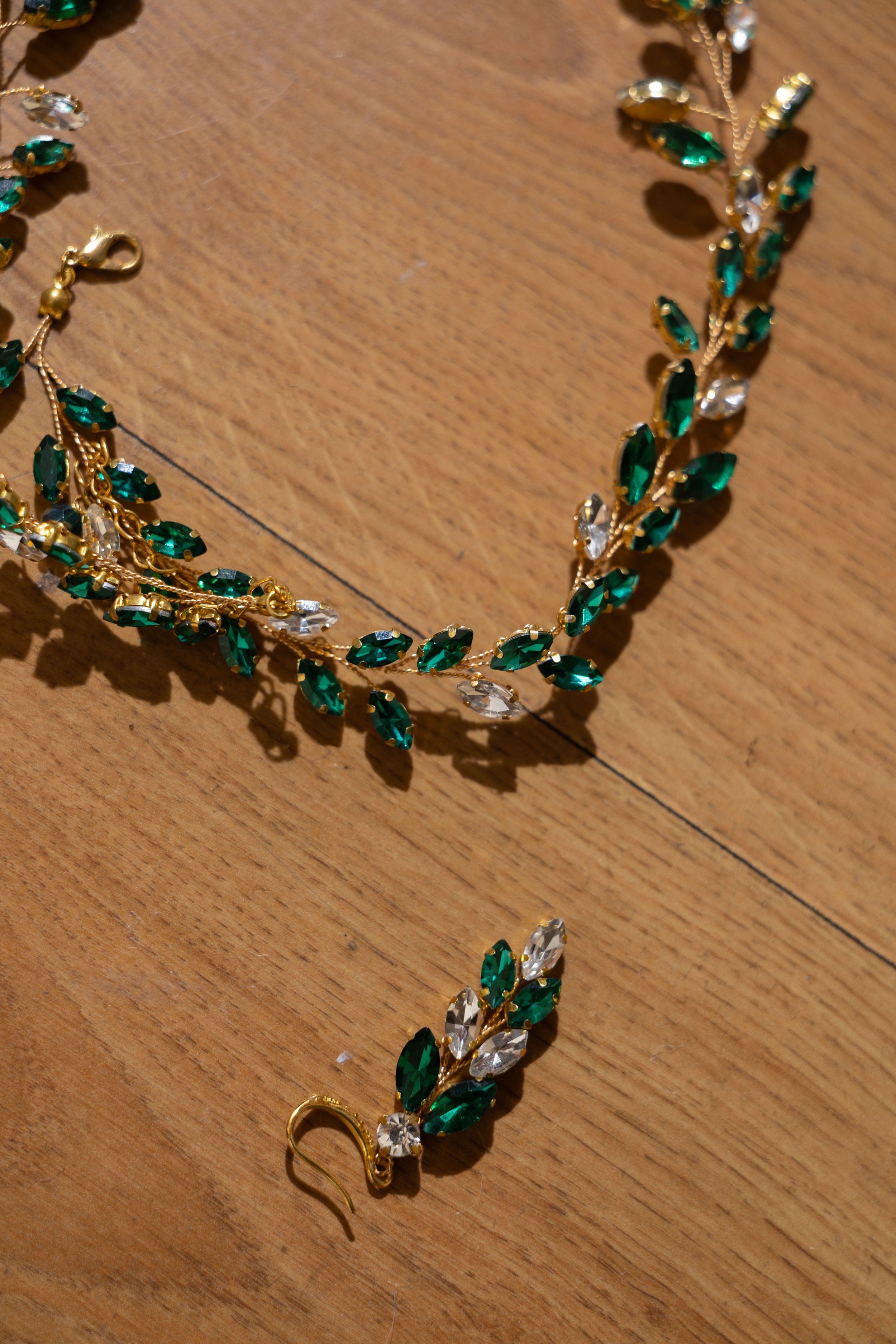 Gold jewelry set consisting of a necklace and a matching earring with green and clear gemstones on a wooden surface.