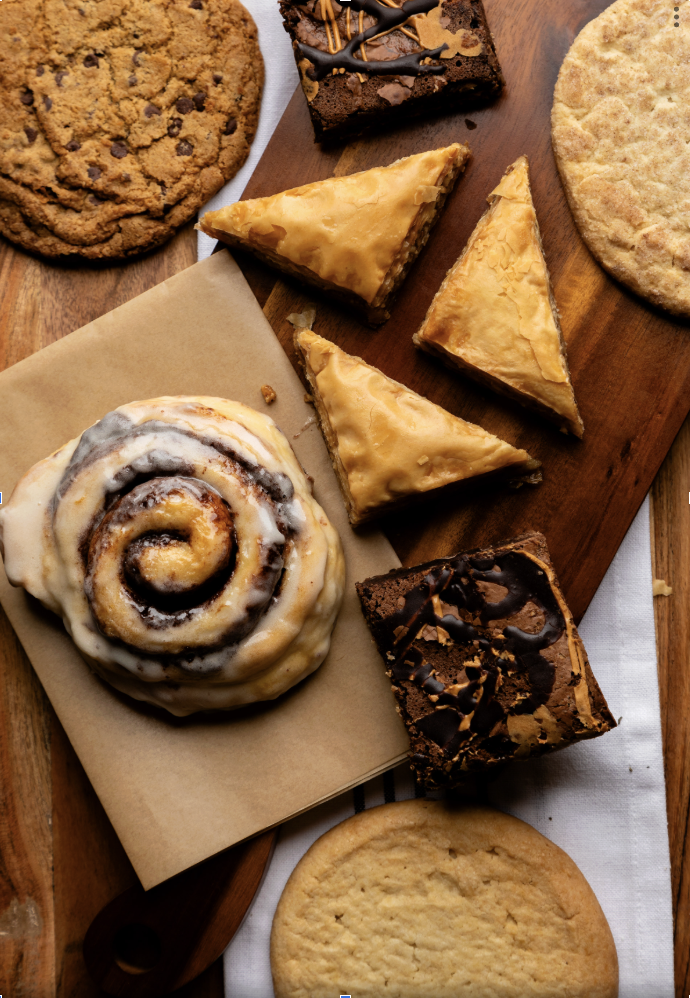 Assorted baked goods including cinnamon roll, chocolate brownies, and sugar cookies on a wooden table.