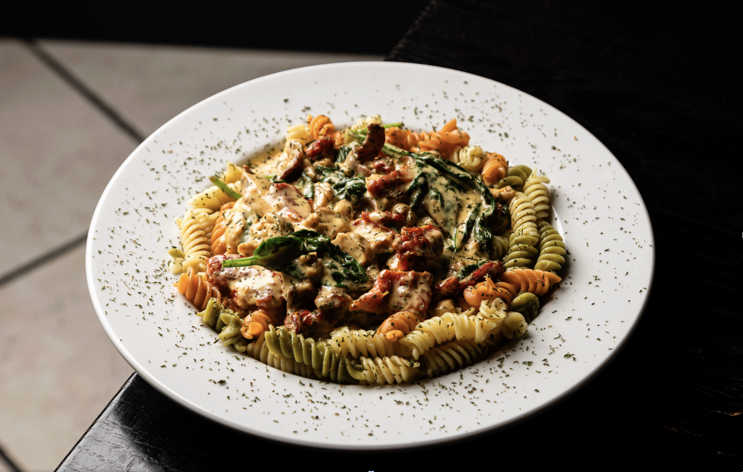 Plate of tri-color rotini pasta with creamy vegetable and meat sauce, garnished with herbs.