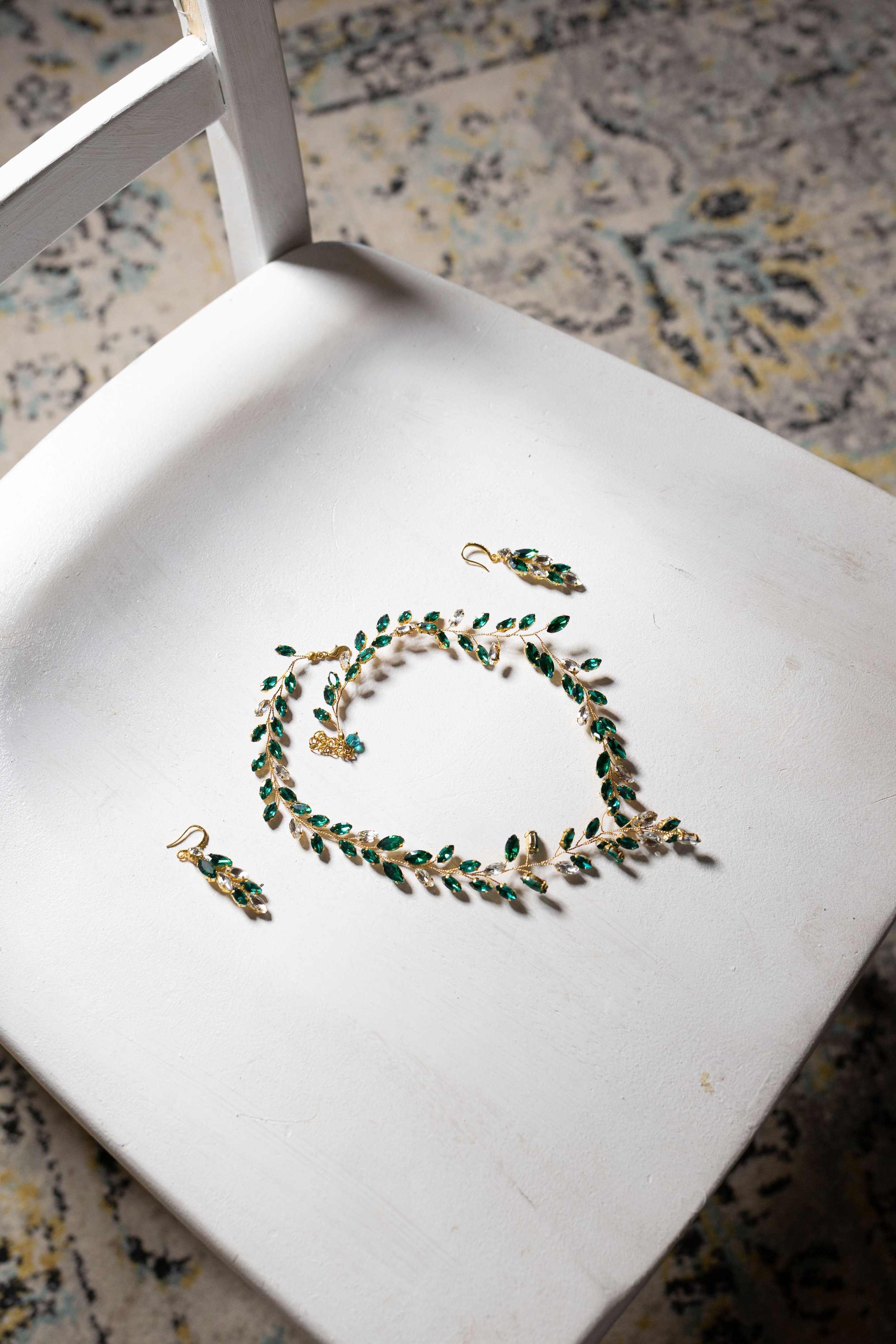 A jewelry set consisting of earrings, a necklace, and a bracelet with green and clear gemstones on a white surface.