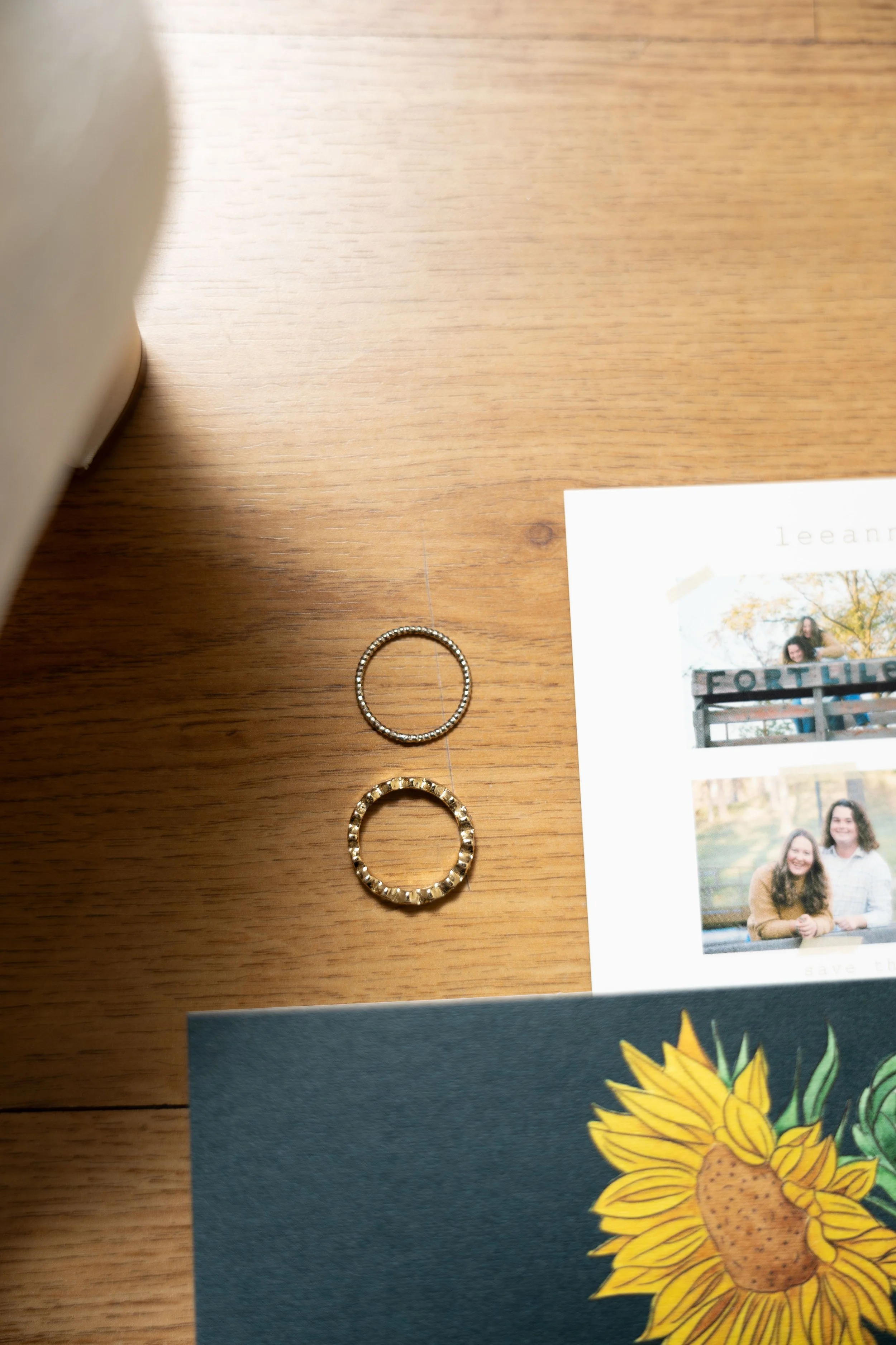 Two rings on a wooden surface with a photograph and a postcard partially visible nearby.