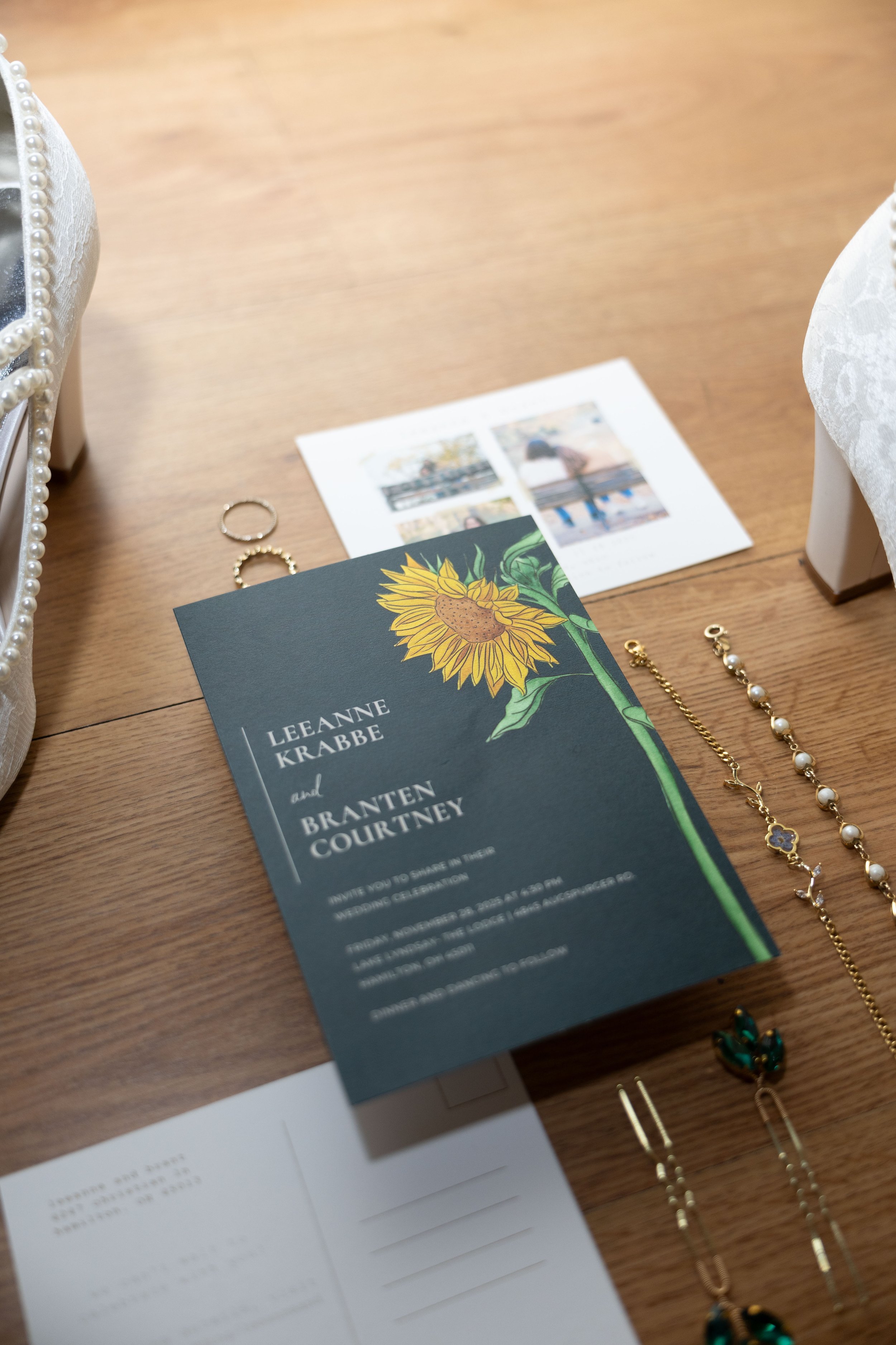 Wedding invitation with sunflower illustration, jewelry including rings, earrings, and bracelets, and a small photo collage on a wooden surface.