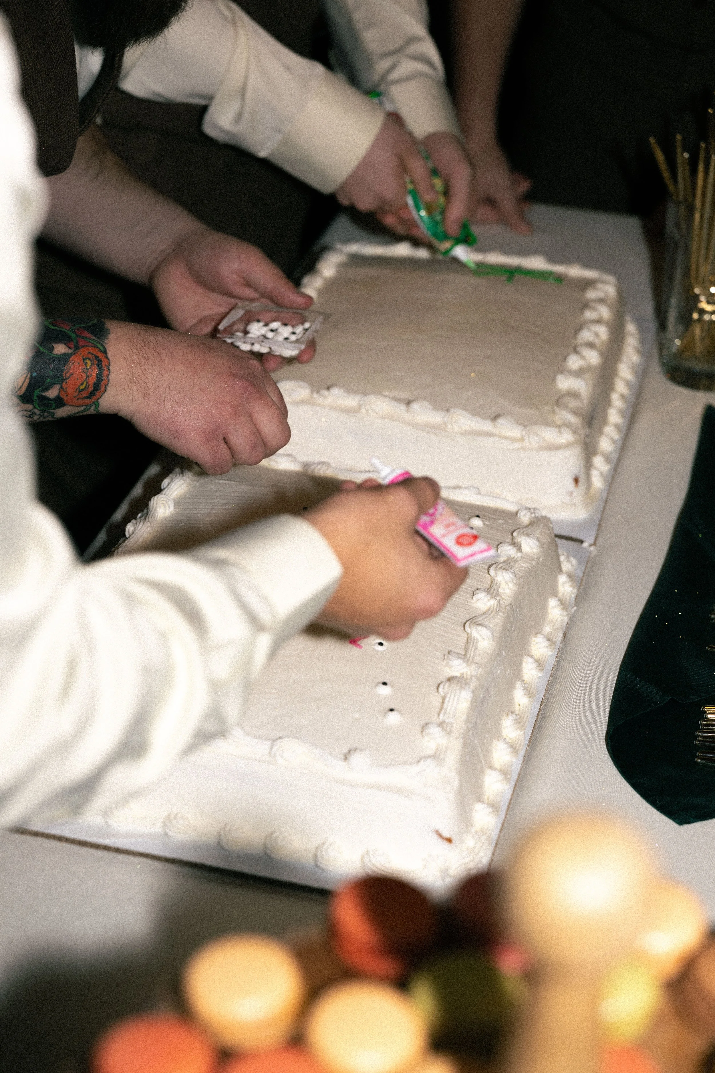People cutting a large white rectangular cake with decorative icing, at a celebration event.