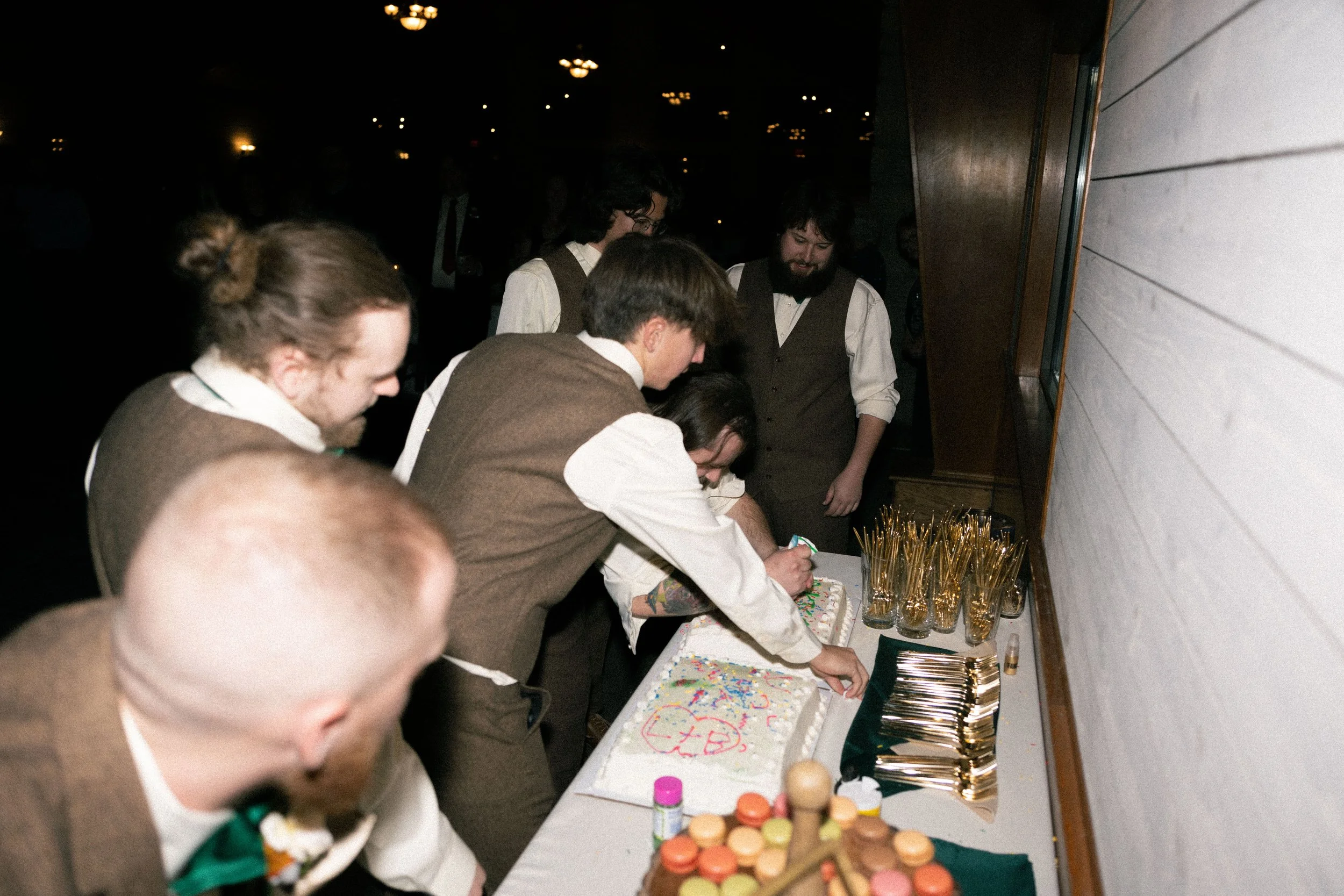 Group of people in vintage attire, celebrating a birthday with a hockey-themed cake, cookies, and drinks in a dimly lit room.