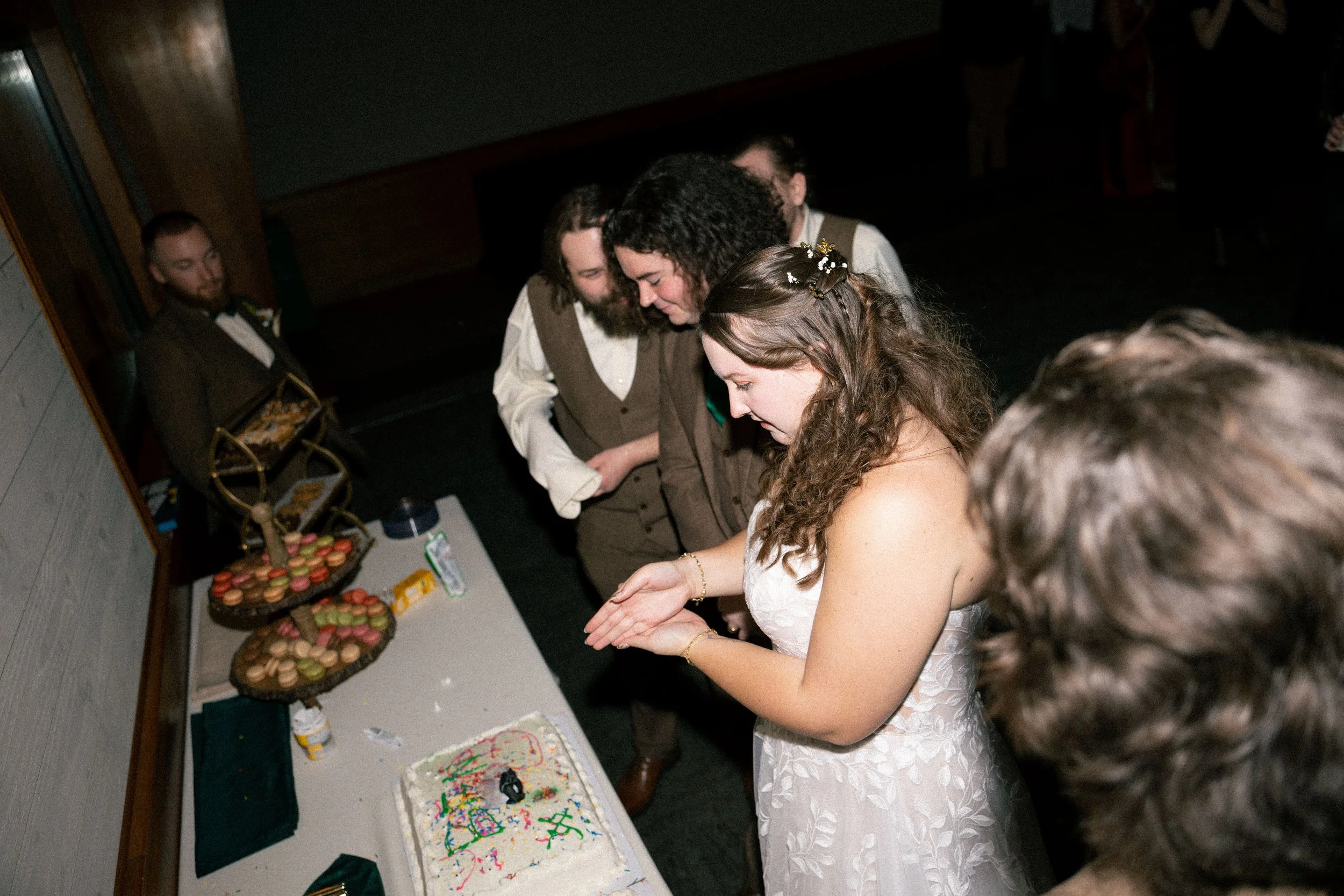 Bride and groom cutting wedding cake surrounded by friends at reception.