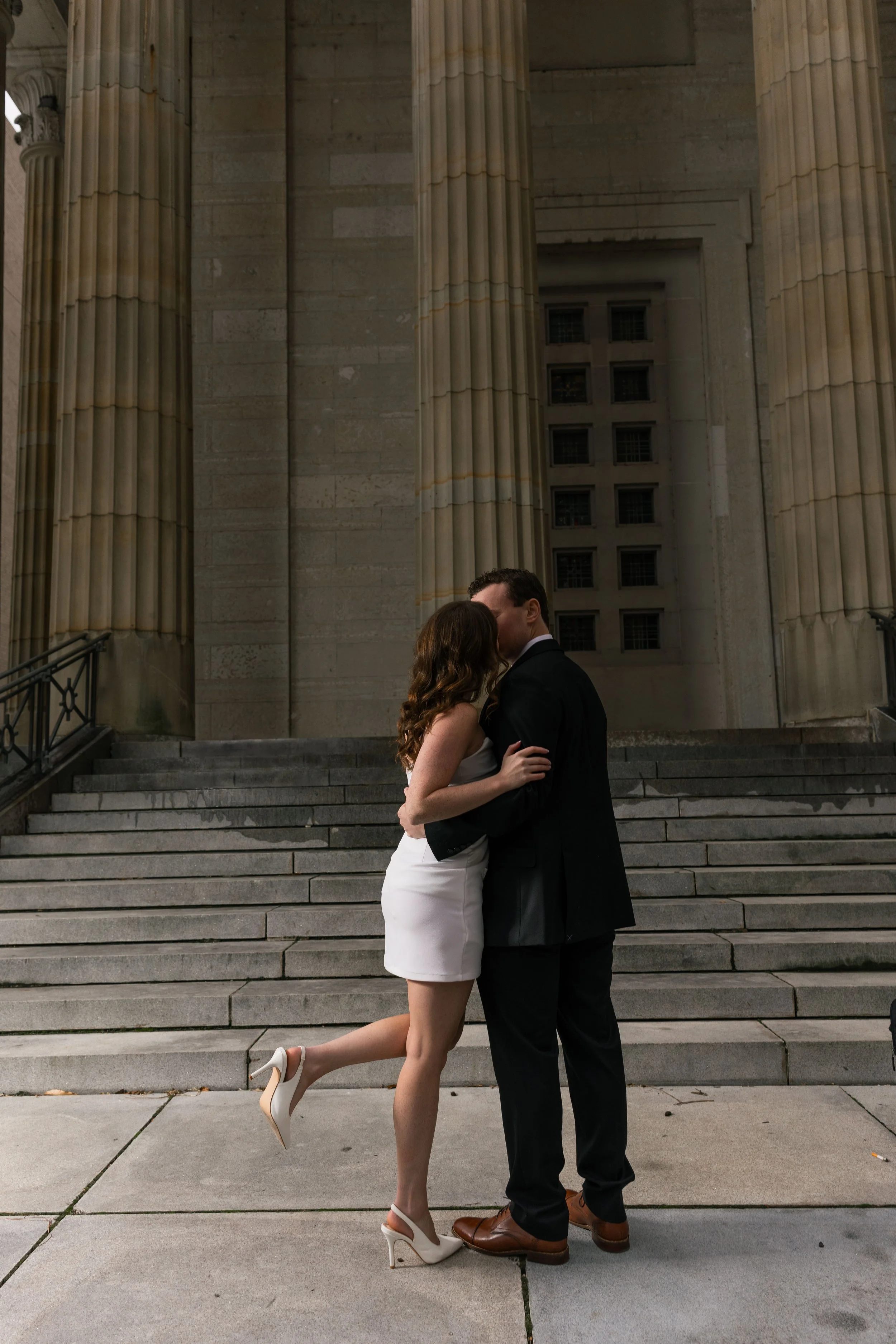 Couple kissing on the steps in front of a historic building with large columns.
