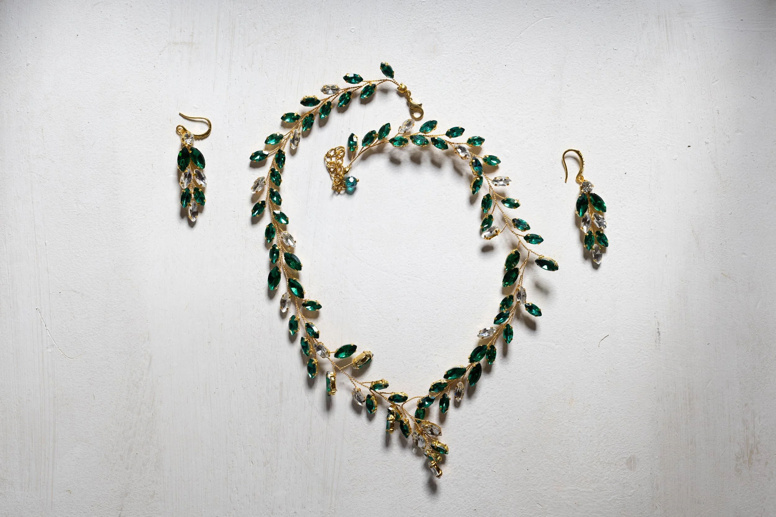 Jewelry set consisting of a necklace and matching earrings with green and clear stones on a white surface.