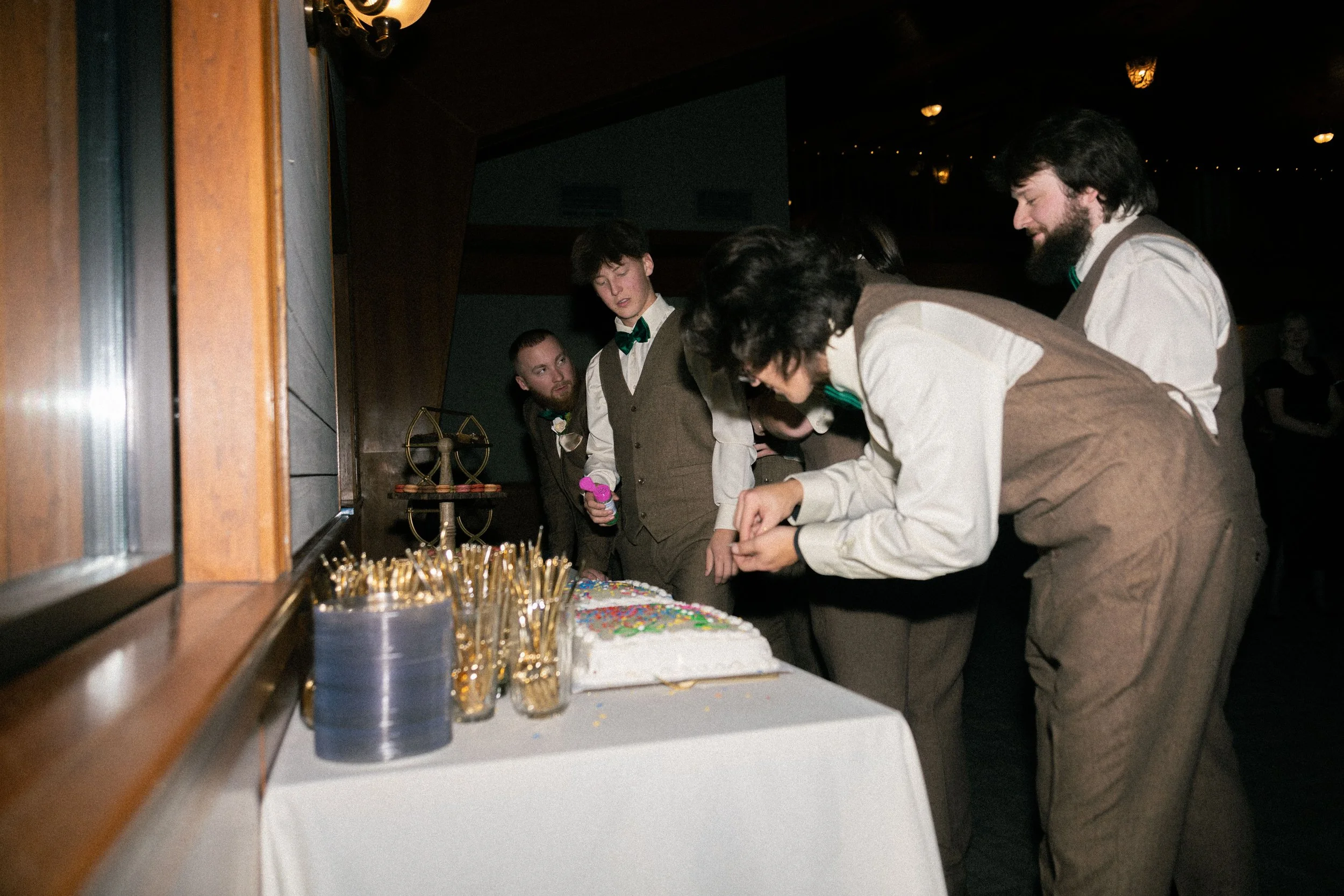 People gathered around a table with a cake in a dimly lit room, preparing to cut the cake during a celebration or party.