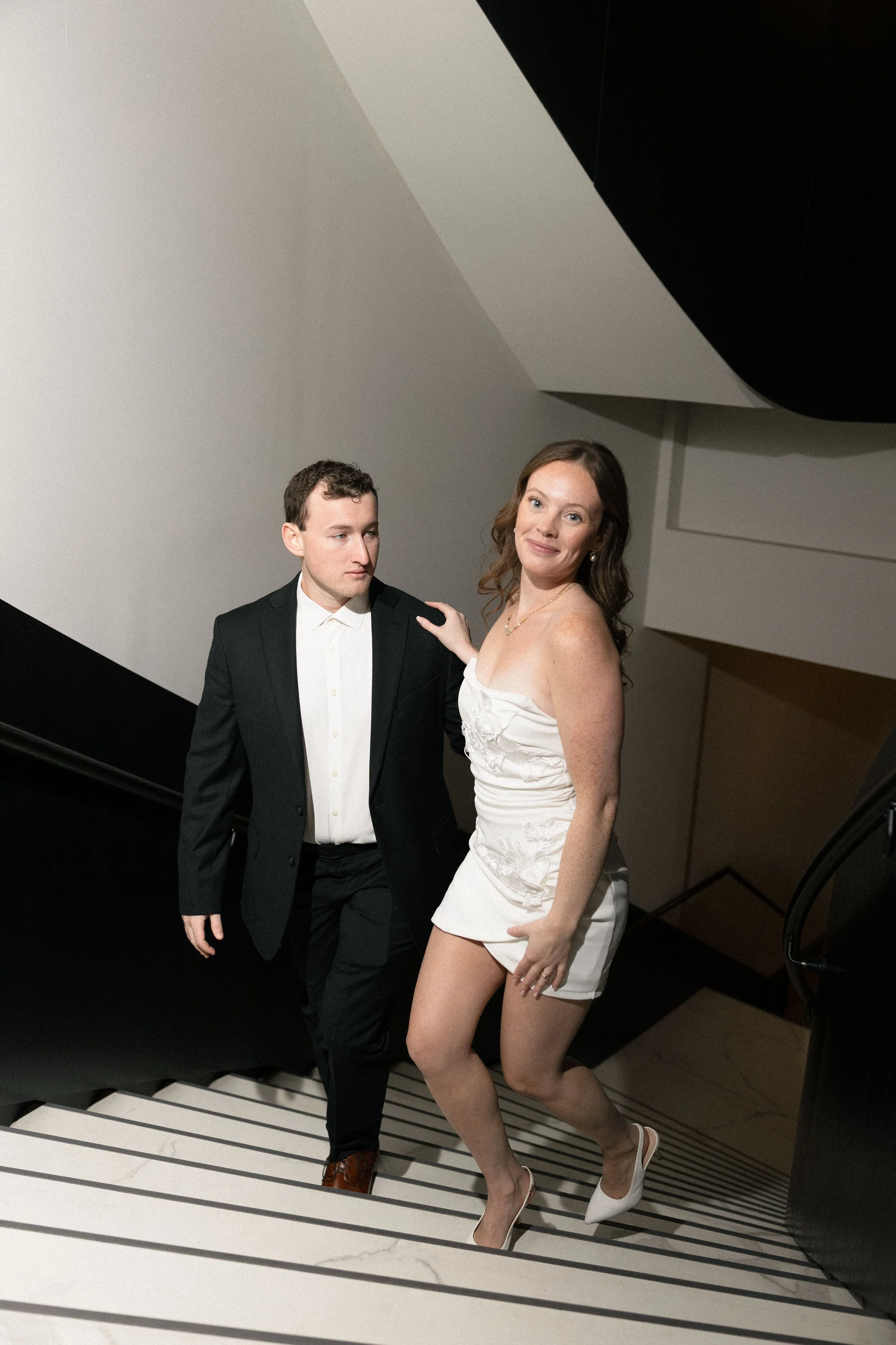 A man in a tuxedo and a woman in a white dress walking up a staircase.