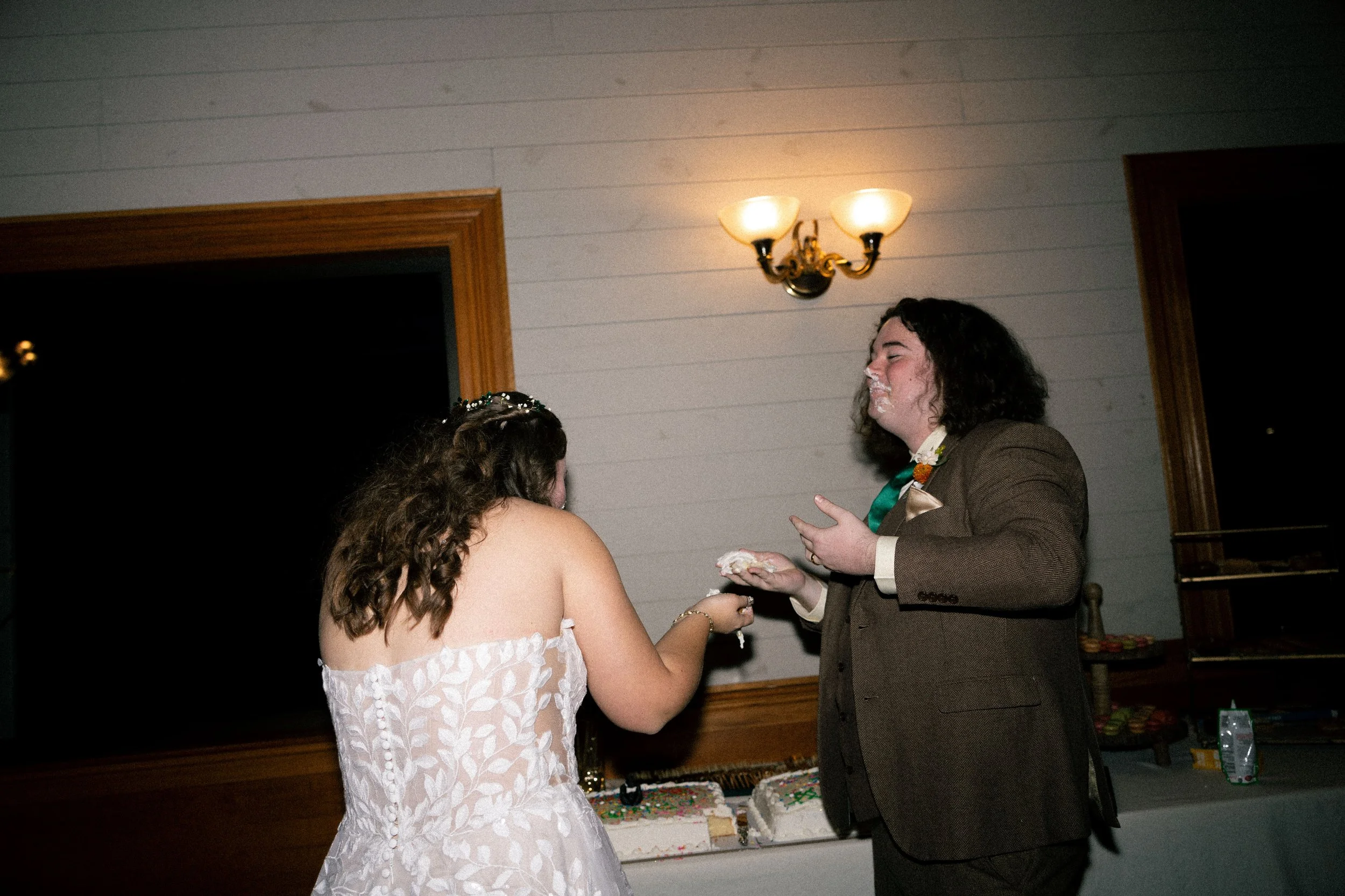 Bride and groom at wedding reception, with groom having cake smushed on his face.