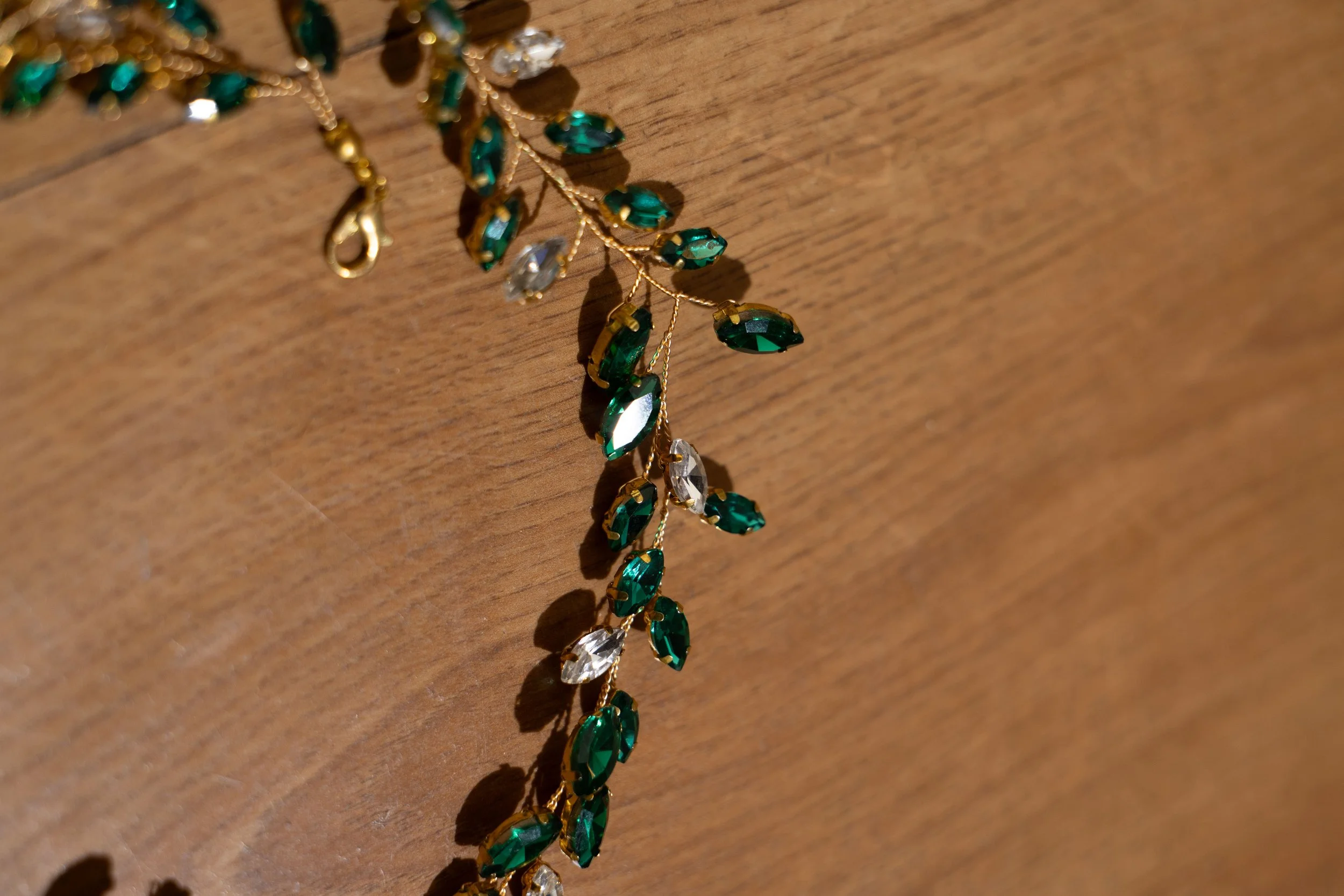 A gold necklace with green and clear gemstone-like beads rests on a wooden surface.