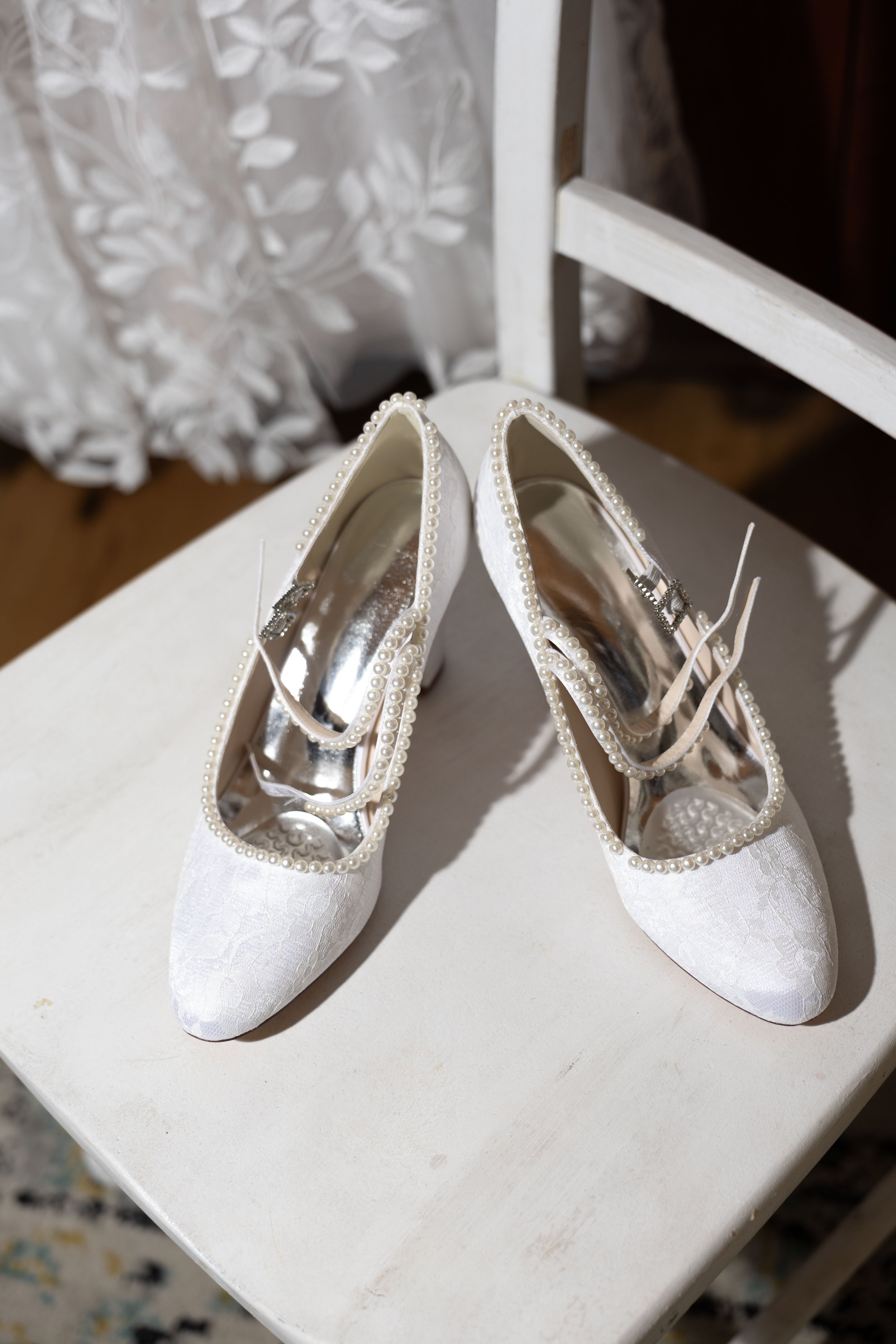 Pair of white wedding shoes decorated with pearls on a white surface.