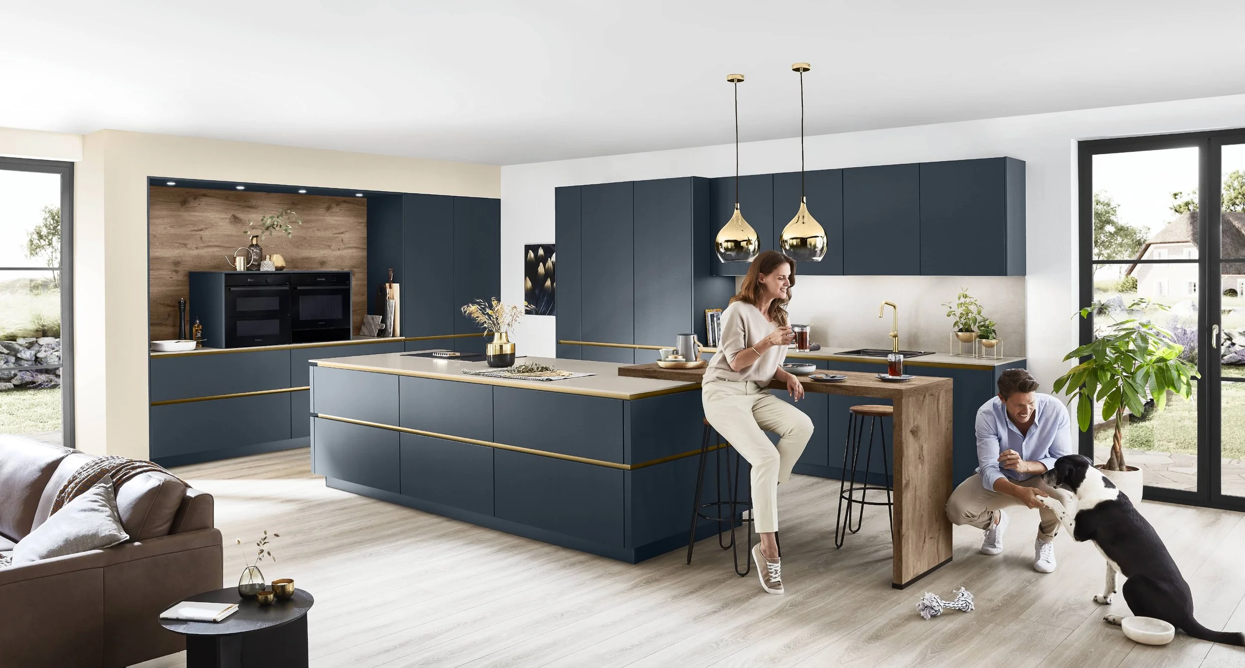 Moderna kök med blå skåp och trädetaljer, två personer med ett hunddjur, stora fönster och ljus träbänkar, samt ett enkelt vardagsrum.