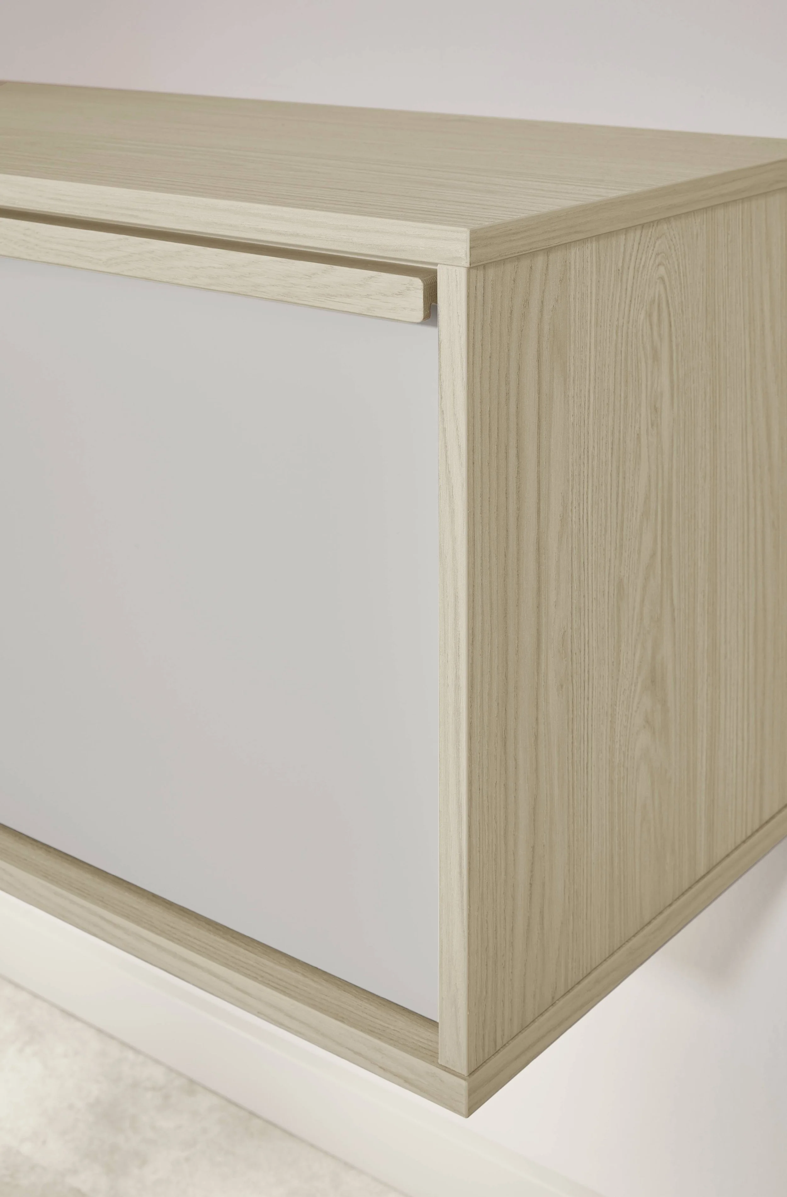 Detalj av ett möbel, troligtvis ett skrivbord eller en byrå, i ljusfärgad trädesign med vit front.