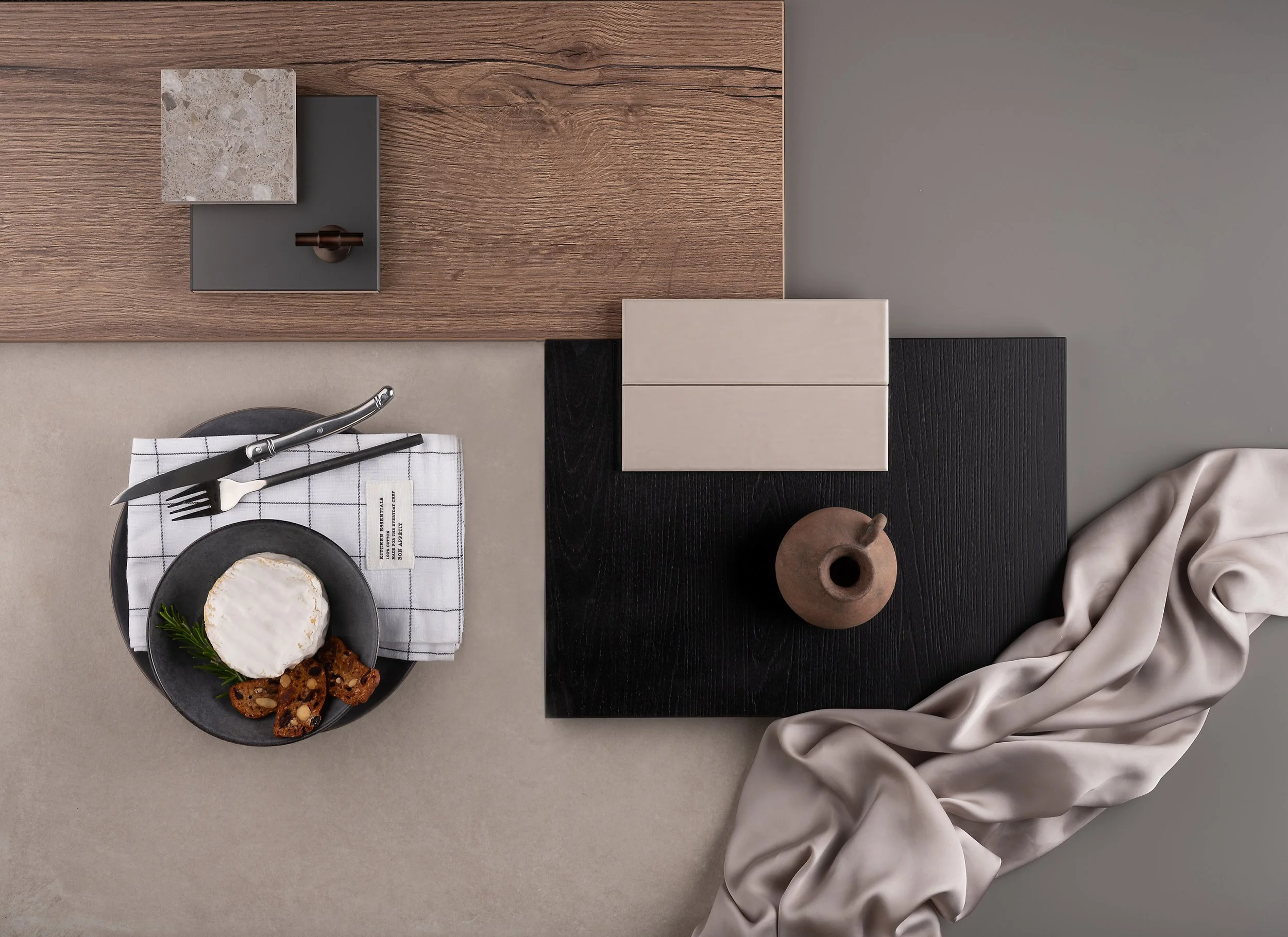 Överheadsbild av ett bord med en ostbricka, kniv och gaffel, samt olika dekorativa föremål som block, vas och tyg.