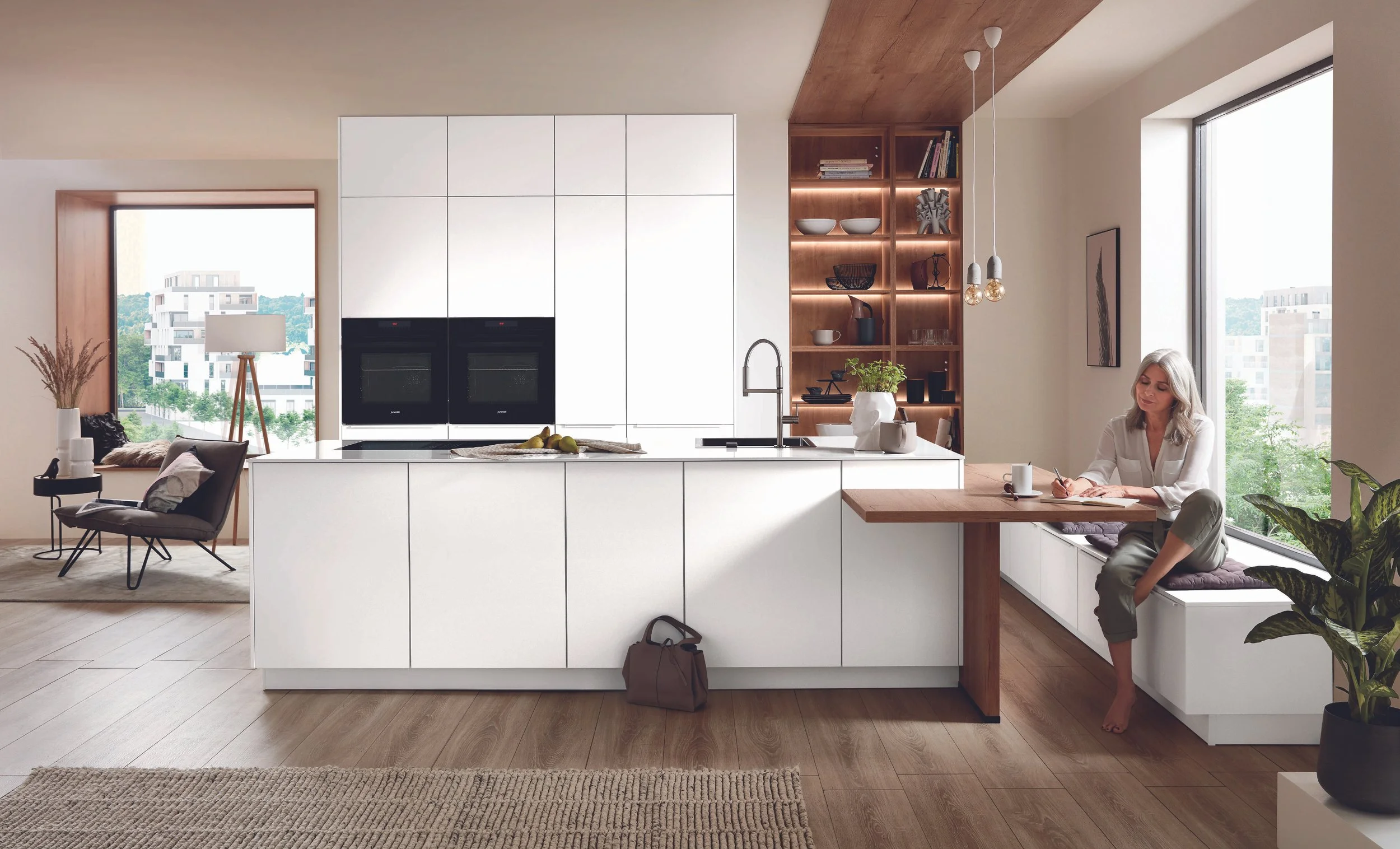 Ett modernt, ljust kök med öppen planlösning, matbord med fyra stolar och ett tv-rum i bakgrunden