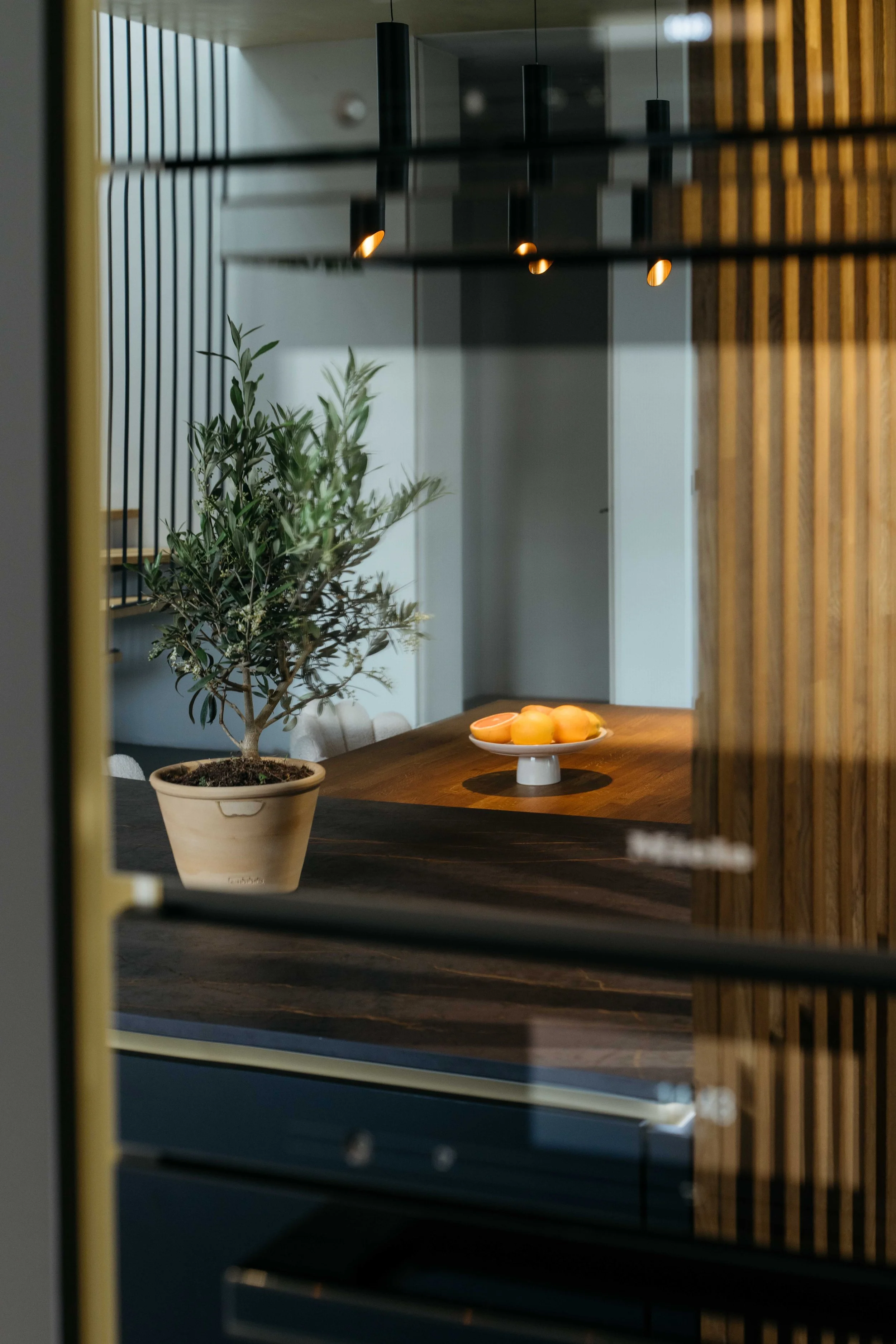 Ett köksbord med en växt i kruka och en skål med apelsiner, omgiven av moderna designinslag i ett hem.