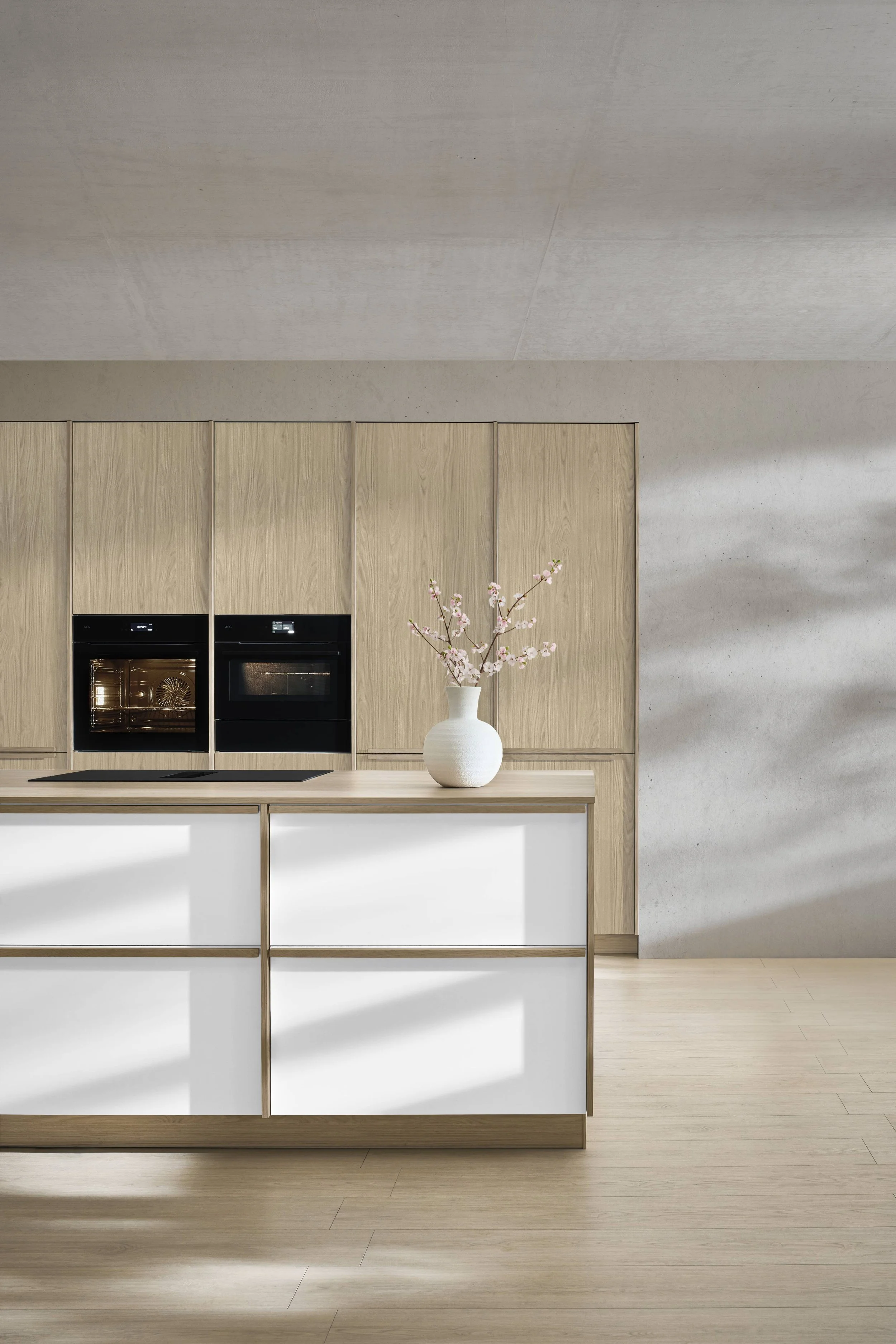 Moderna kök med inbyggda ugnar, ett vitt köksö med skåp, träluckor, ett dekorativt blompannk i keramik och luftiga, ljusa kläddes av golv och väggar.