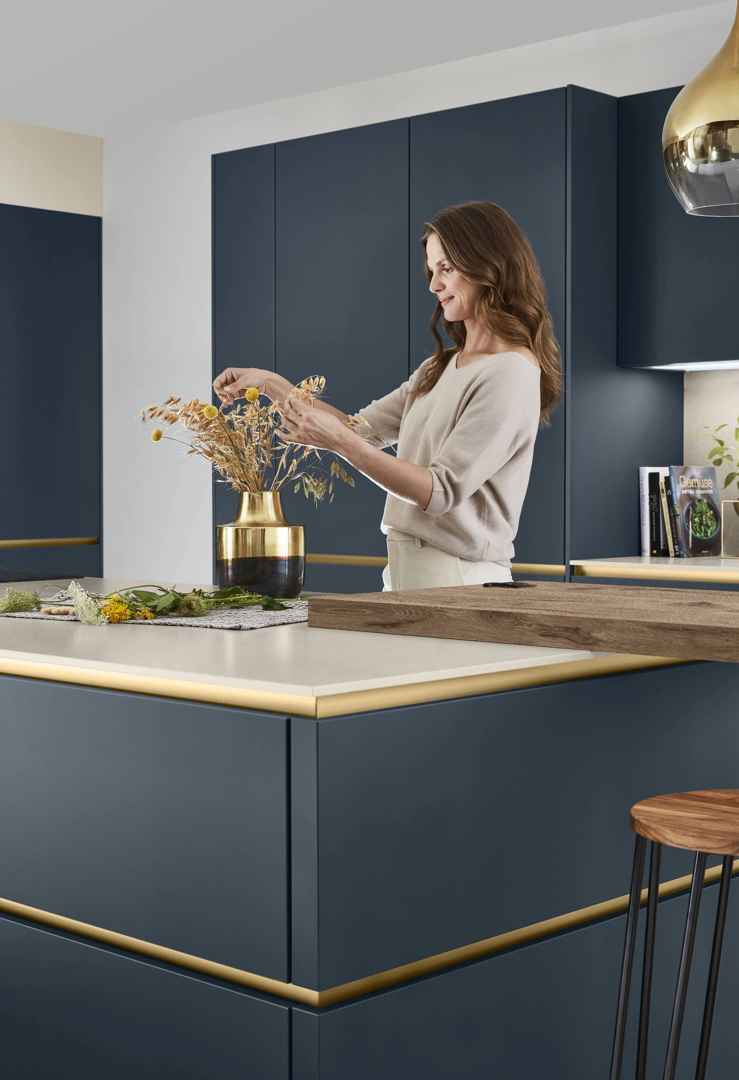 Kvinnor i ett modernt kök arrangerar en blomsterbukett i en guldfärgad vas.