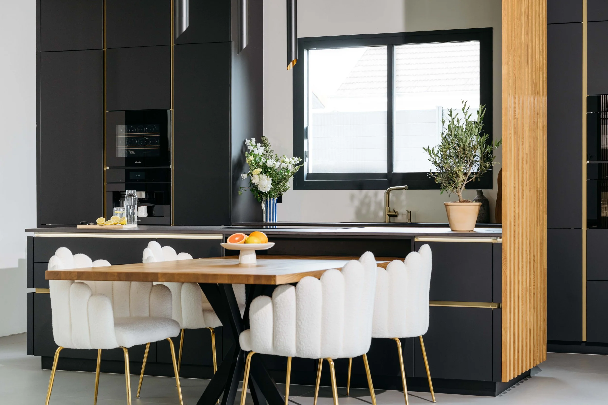 Kök med svartskåp, ett träbord med vita stolar, ett fönster och bladväxter.