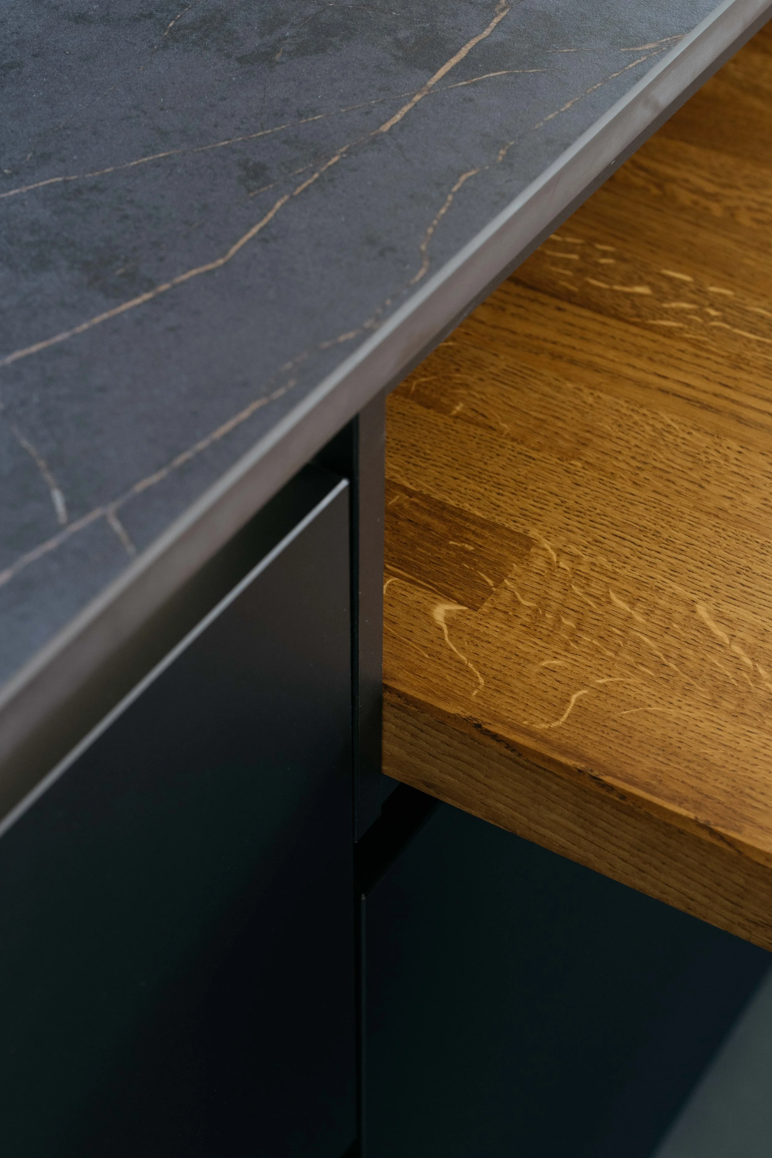 Närbild av ett köksskåp med en mörkgrå marmorskiva på toppen och ett trähölje.