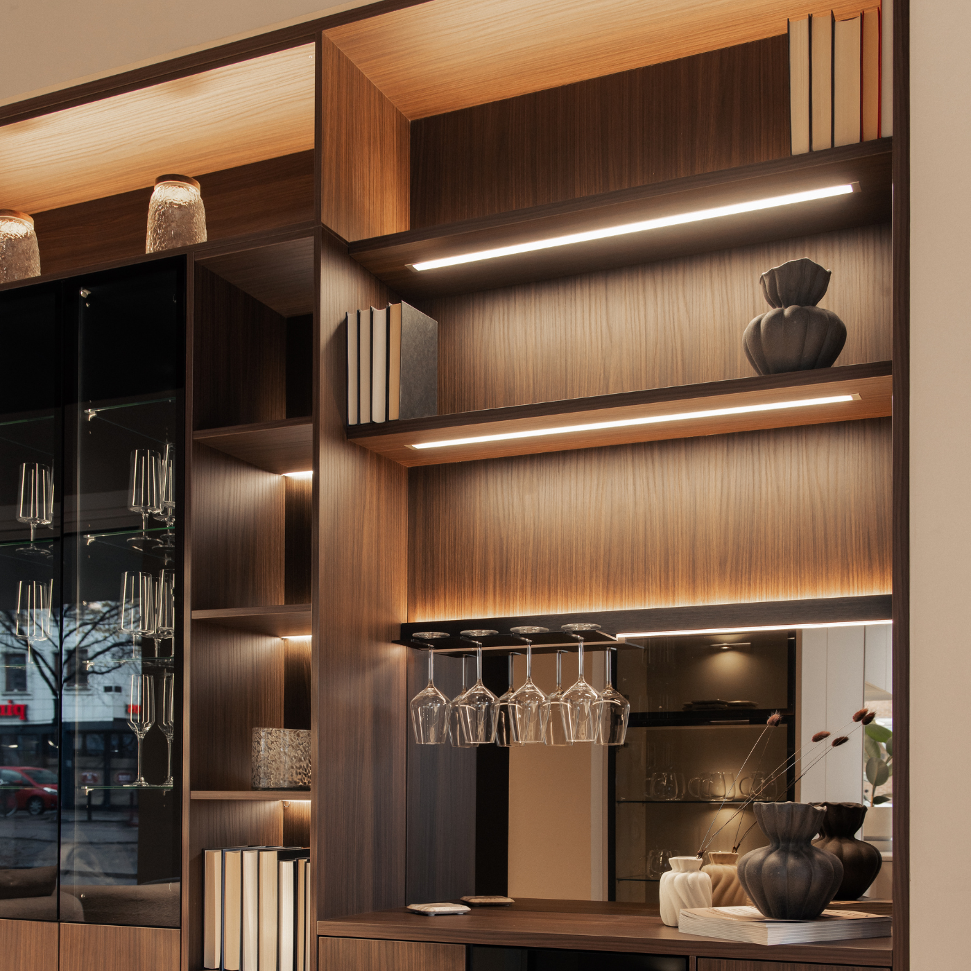 En träskåpvägg med böcker, vaser och glasrum, inbjudande inredning med belysning.