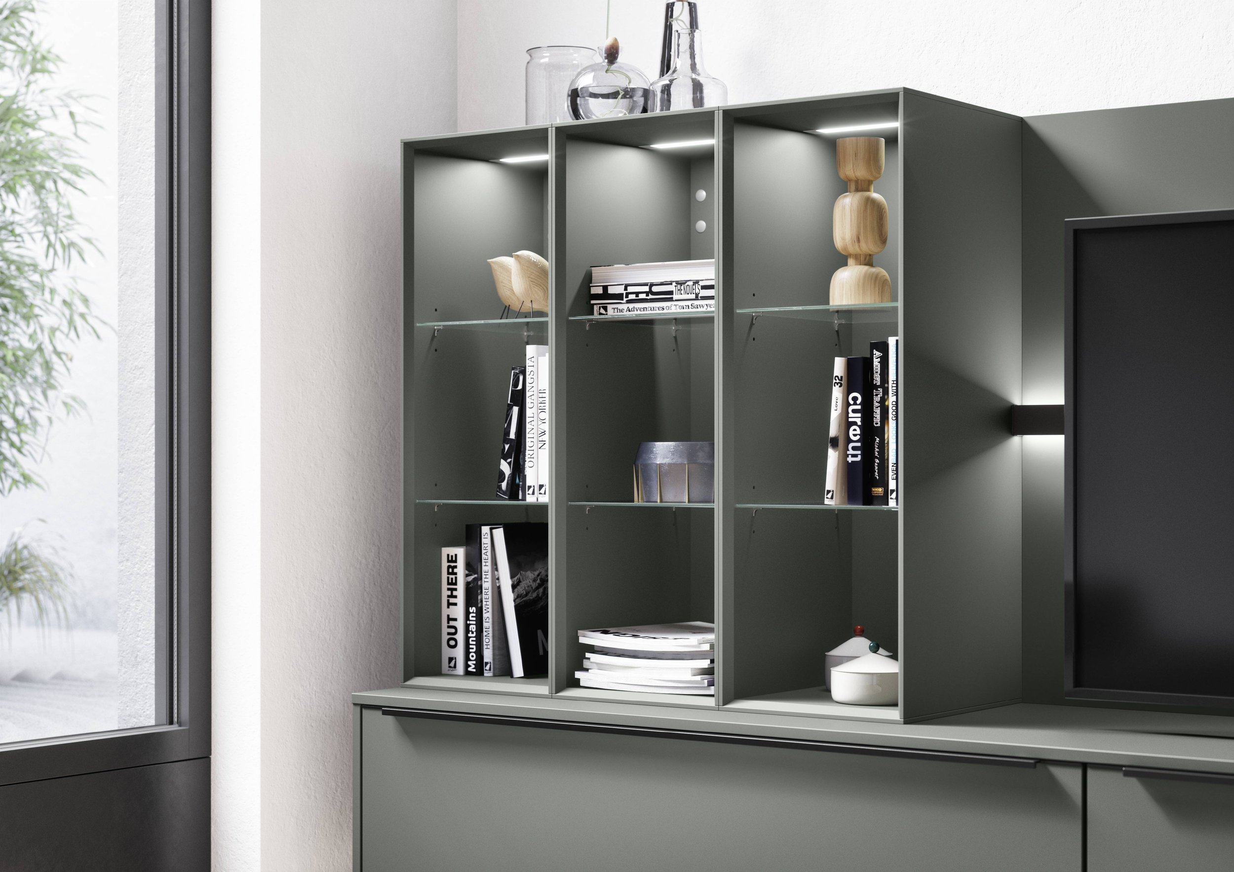 Grå hylla med böcker och dekorativa föremål, i ett modernt inrett vardagsrum.