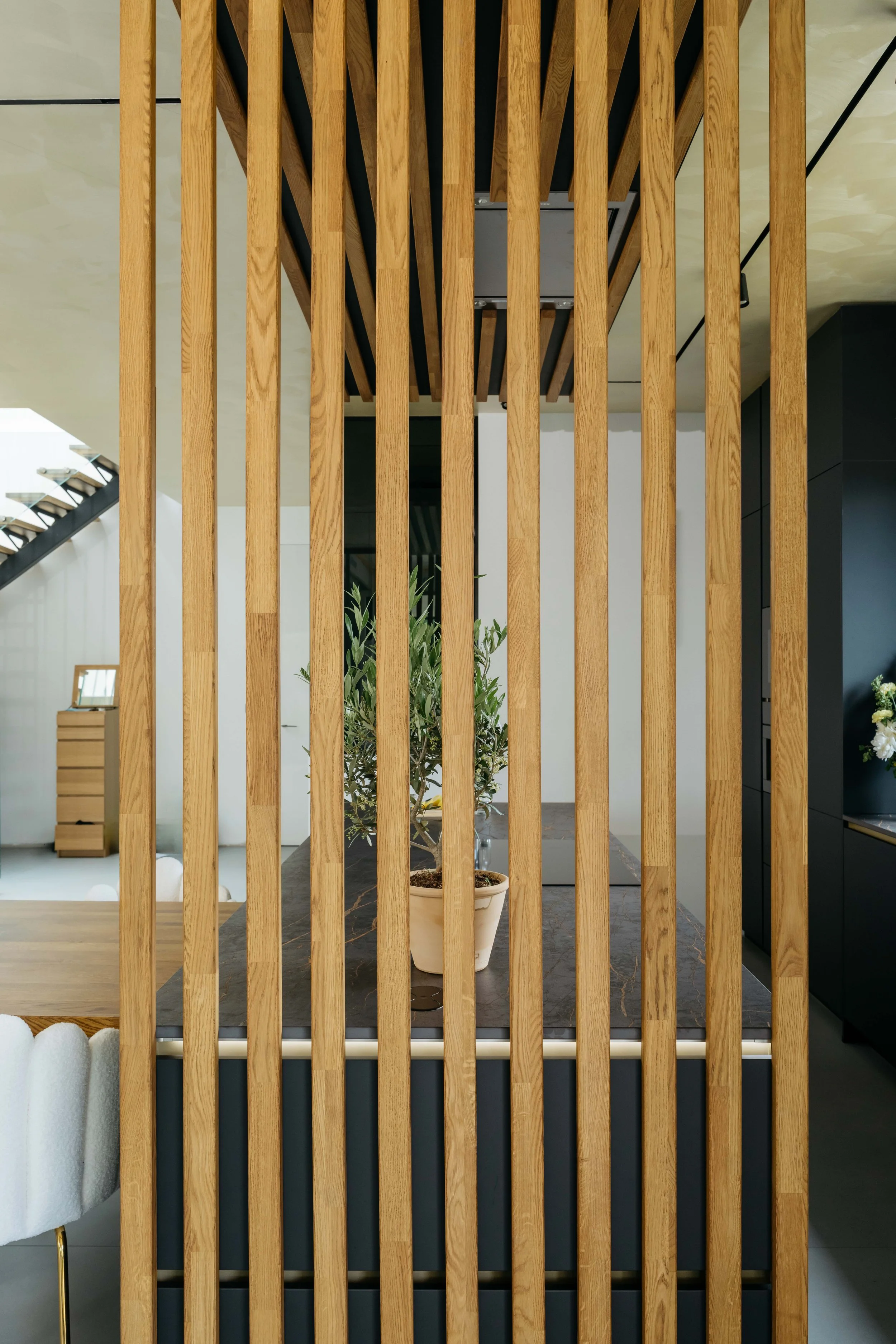 En växt i en kruka bakom en träskärm i ett modernt inrett rum.