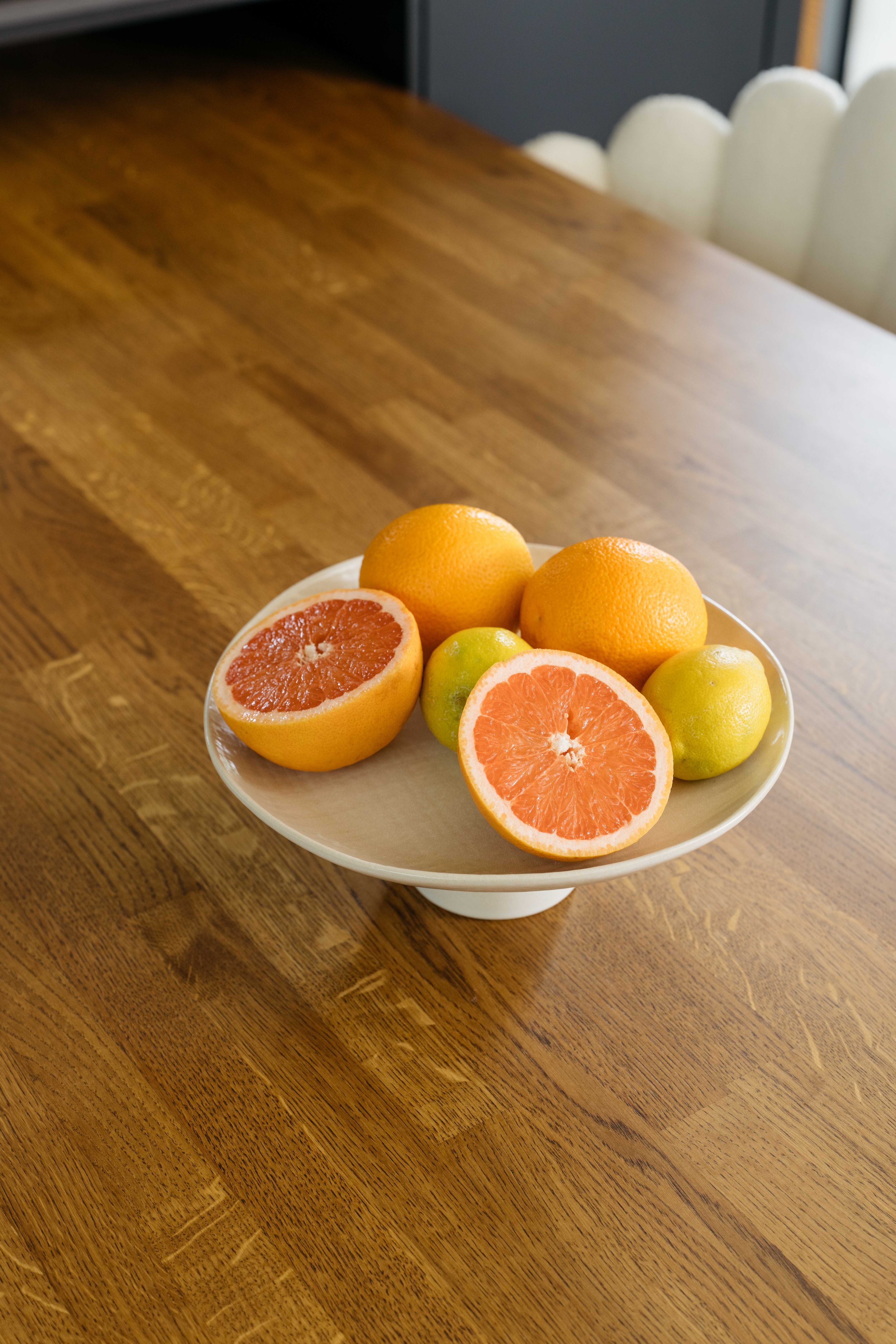 En vit skål med olika citrusfrukter, inklusive halverade och hela grapefrukter, på ett träbord.