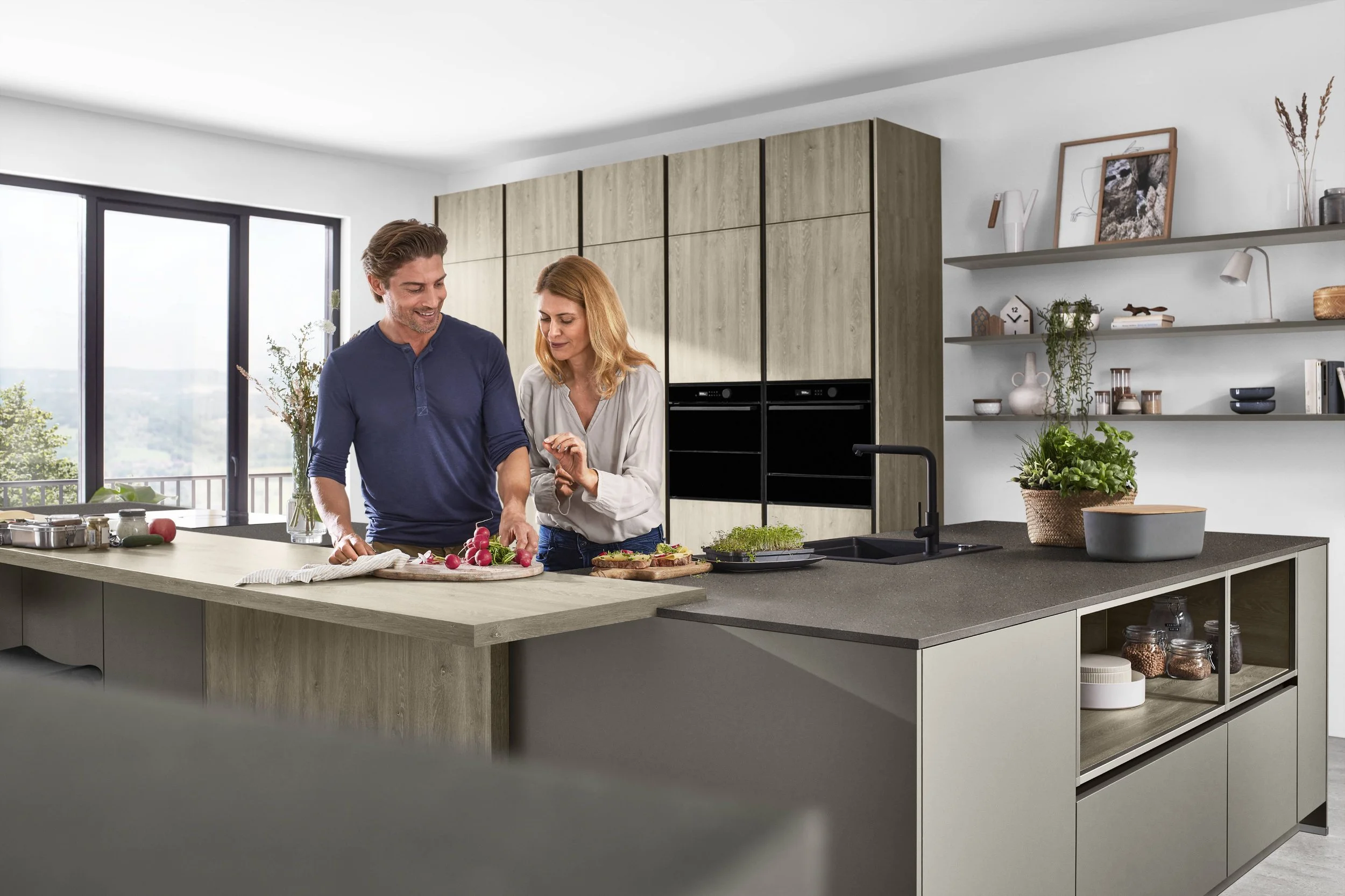 Två personer i ett modernt kök förbereder mat tillsammans, en man och en kvinna som står vid ett köksbord med mat och grönsaker.