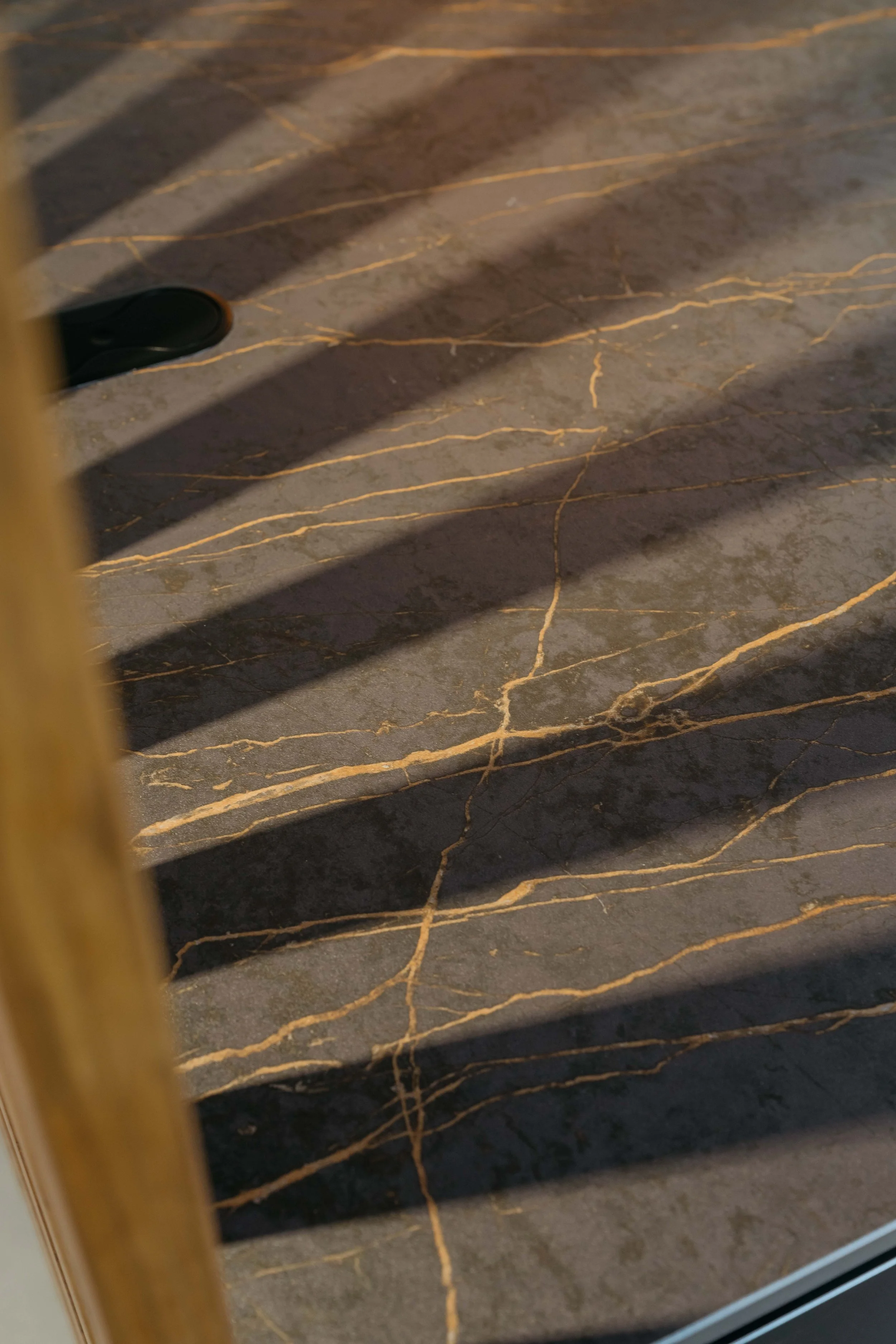 Närbild av ett golv med mörkgrå marmor med gyllene ådror och skuggor av spaljérade ljus.