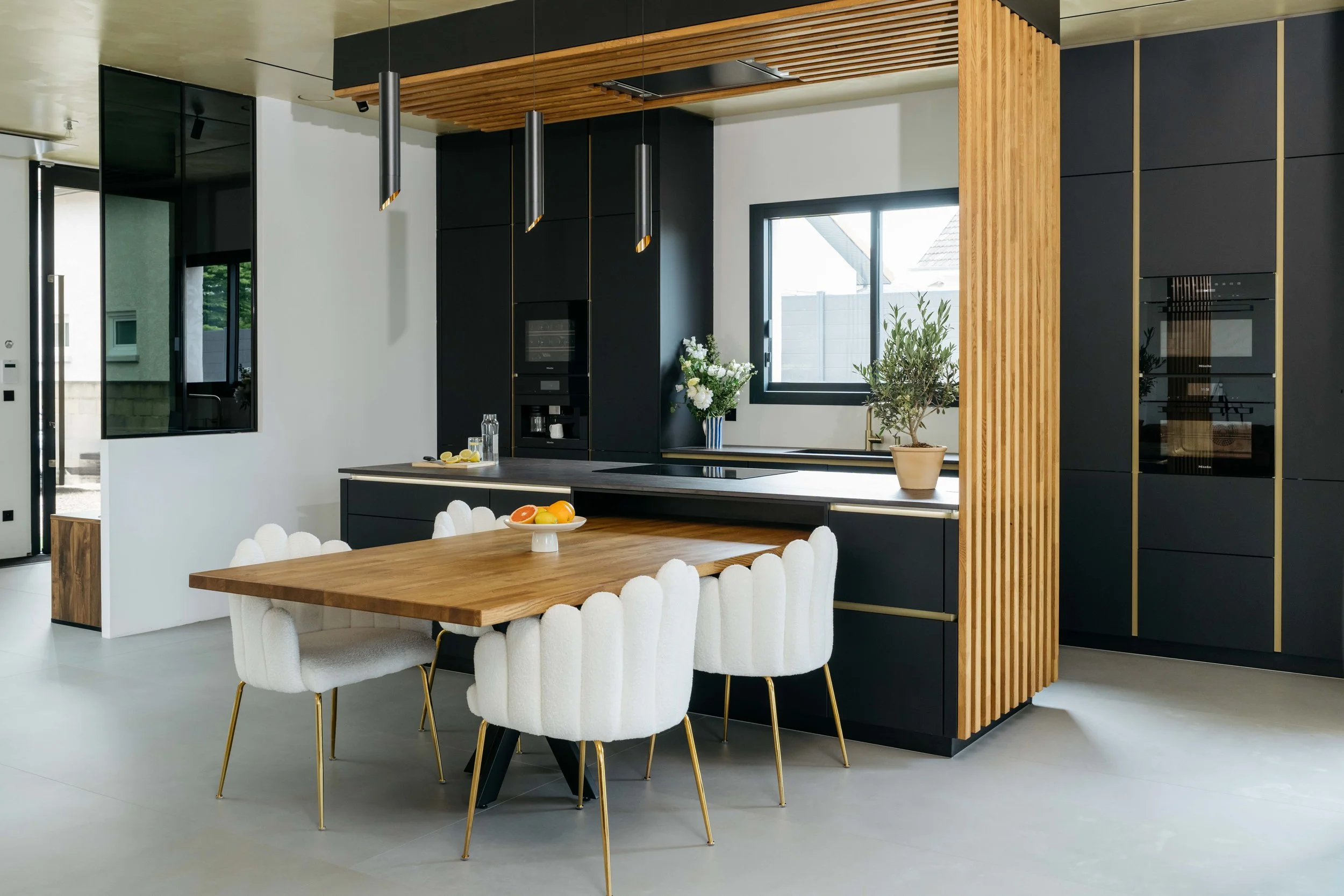 Moderne kök med svart och trädetaljer, ett matsalsbord med sex vita stolar och dekorationer, samt växter på fönsterbänken.