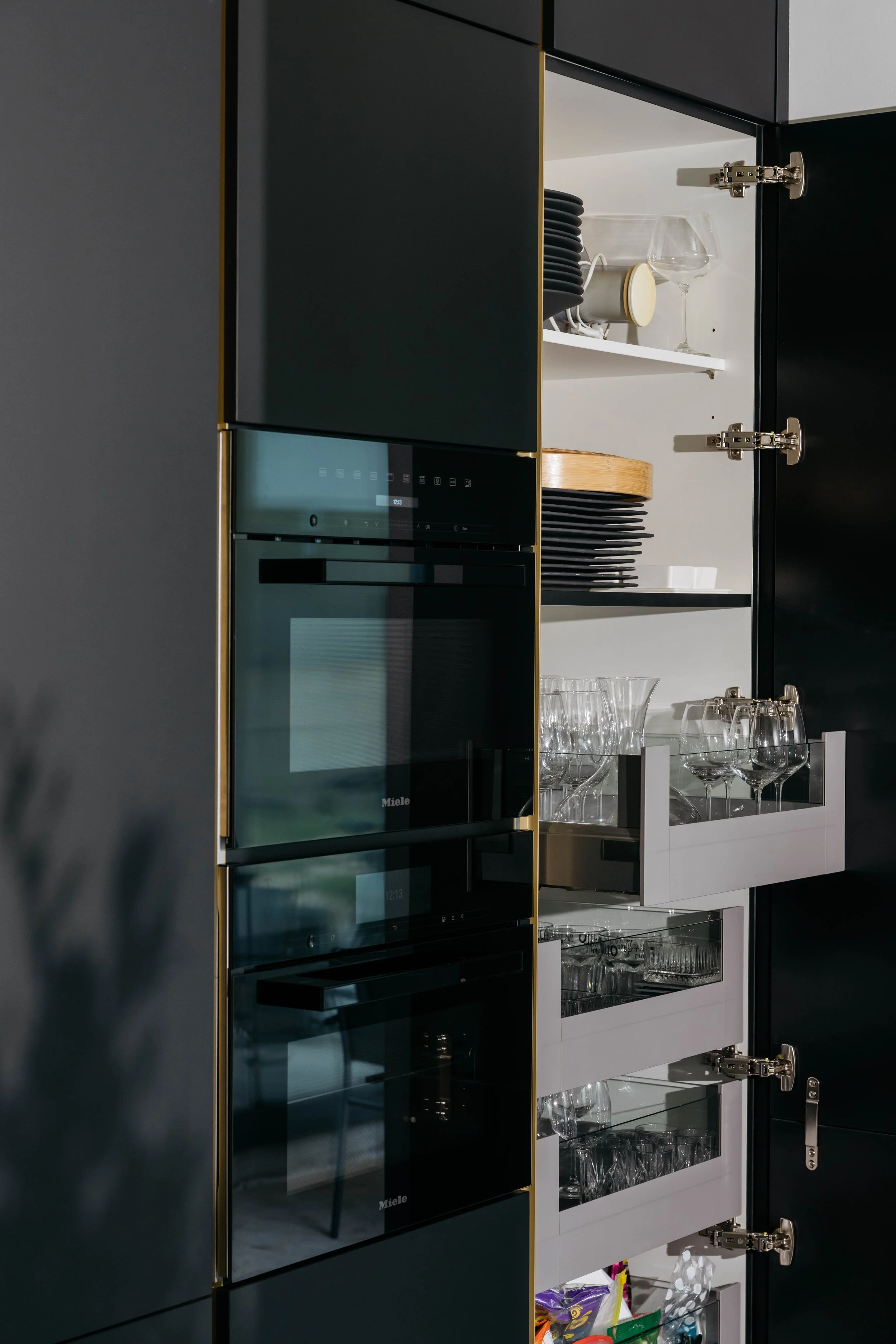 Öppen kökskåp med glasdörrar, serveringsglas och tallrikar inuti.