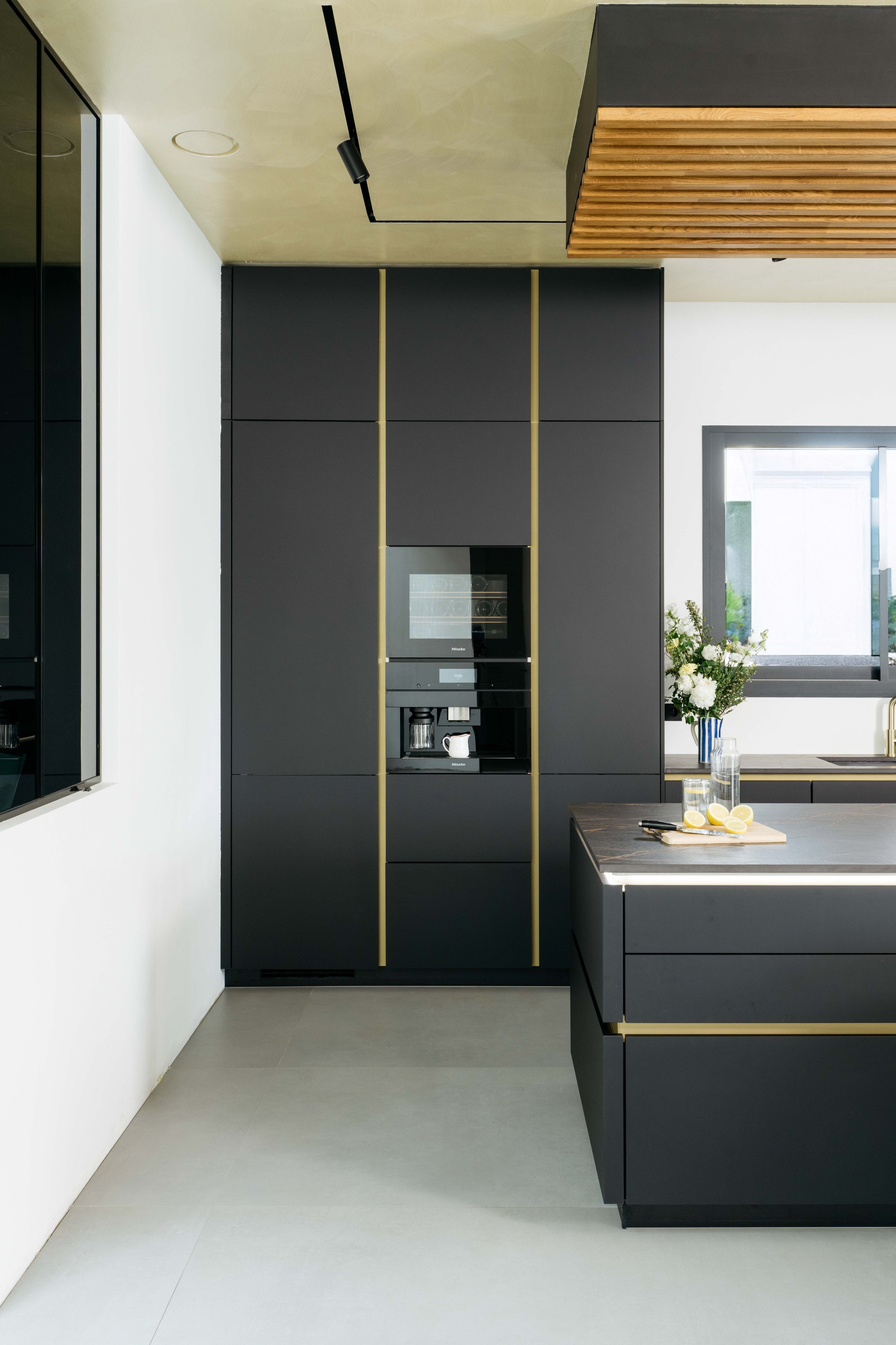 Modern köksinredning med svart skåp, brunt trädetaljer på taket och ett vitt köksbord med citroner och dricksglas.