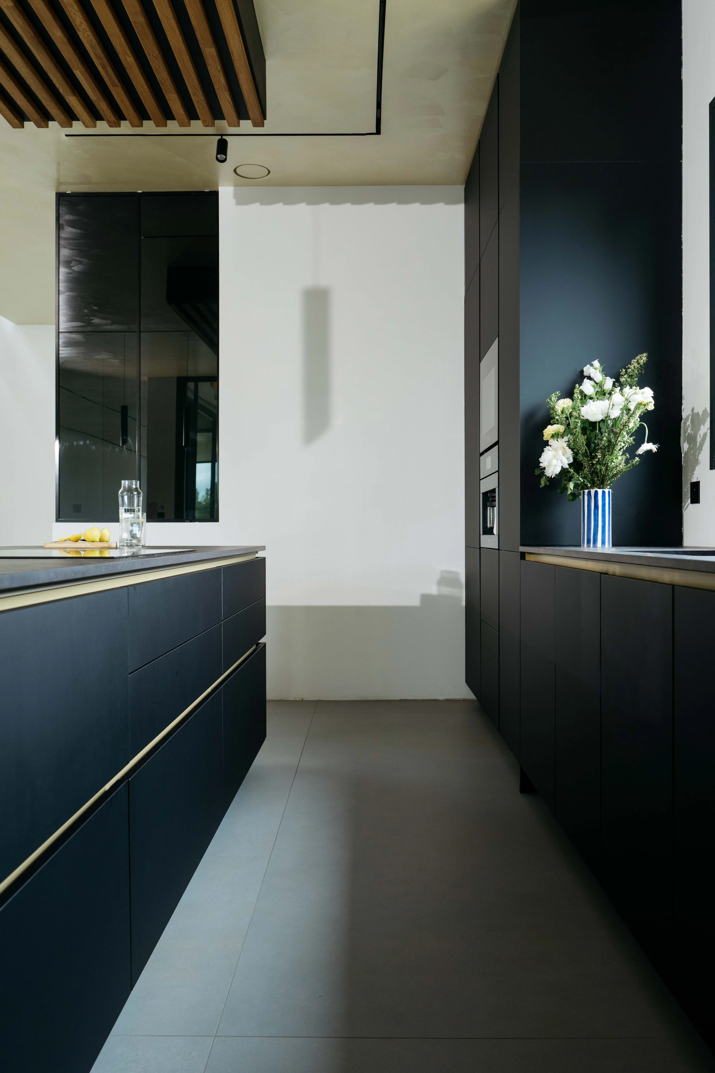 Modernt kök med svarta skåp, en blomma i ett blåvitrutigt vaser och ett glas vatten på diskbänken.