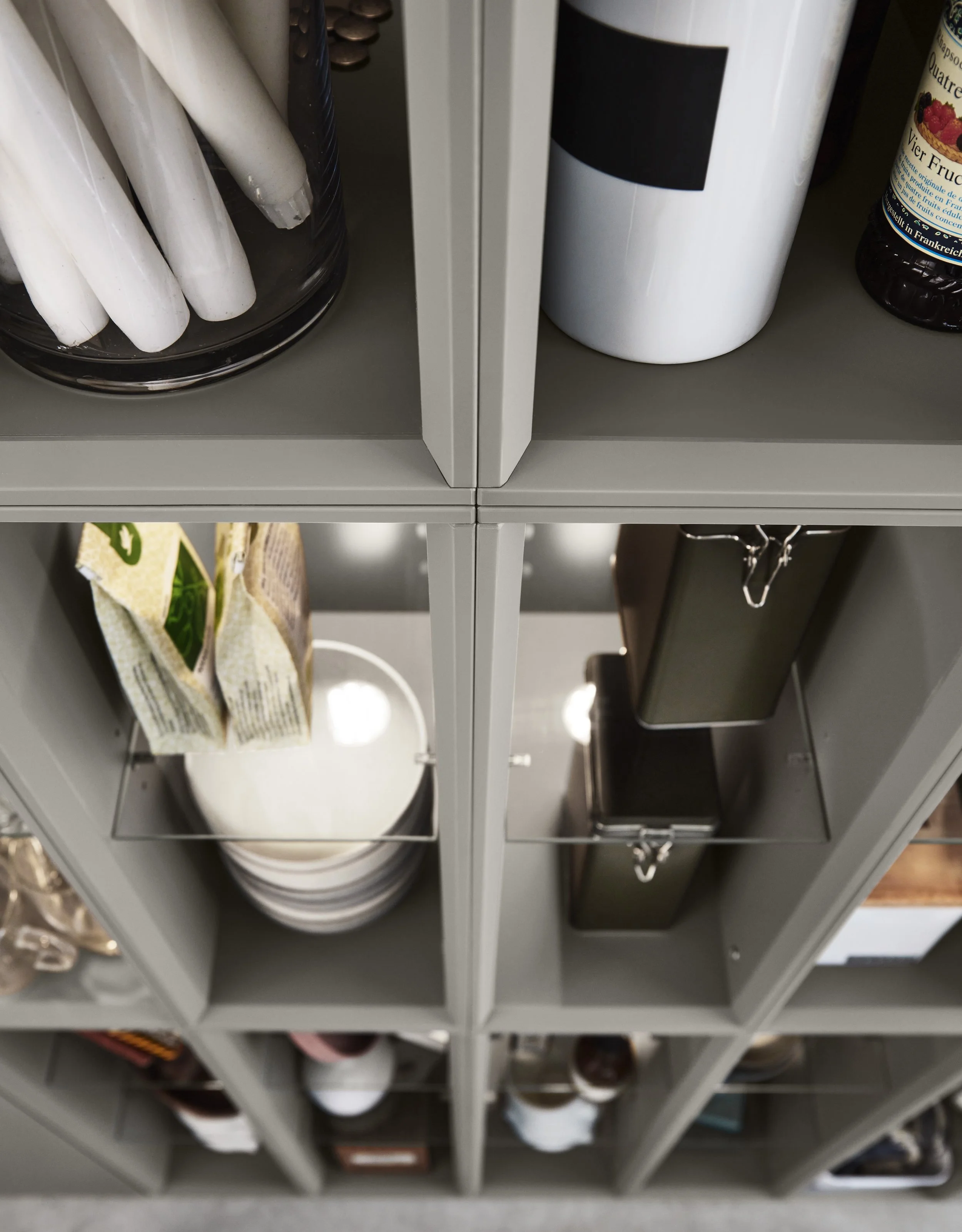 Svart hyllplan med rack av små skåp med cereklampar, burk, böcker, koppar, porslin och påsar.