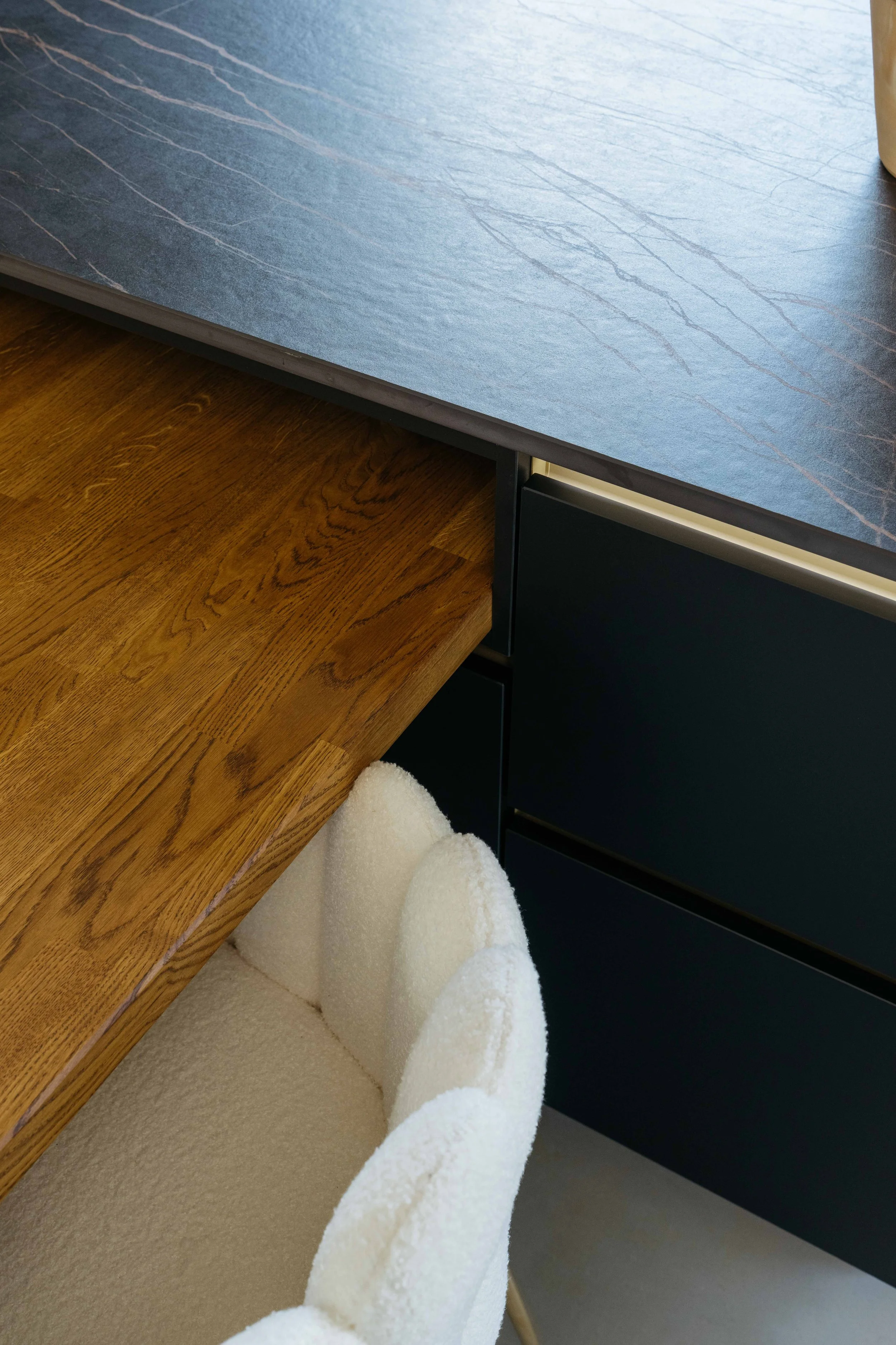 Del av ett bord med blå yta, ett skåp och en vit, mjuk stol.