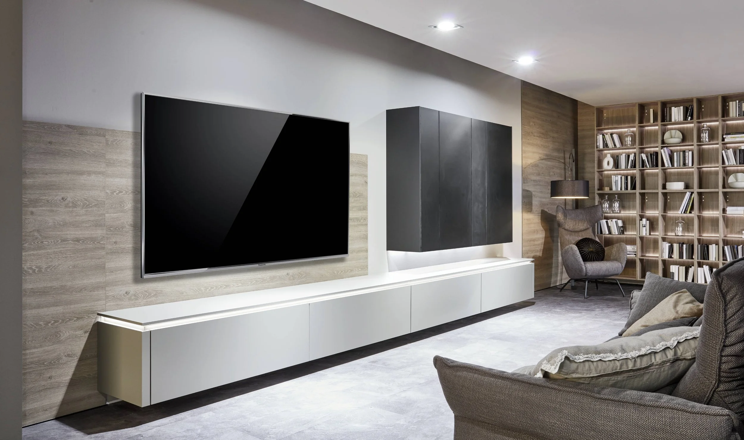 Modernt vardagsrum med väggmonterad TV, bokhylla, soffor och fåtöljer.