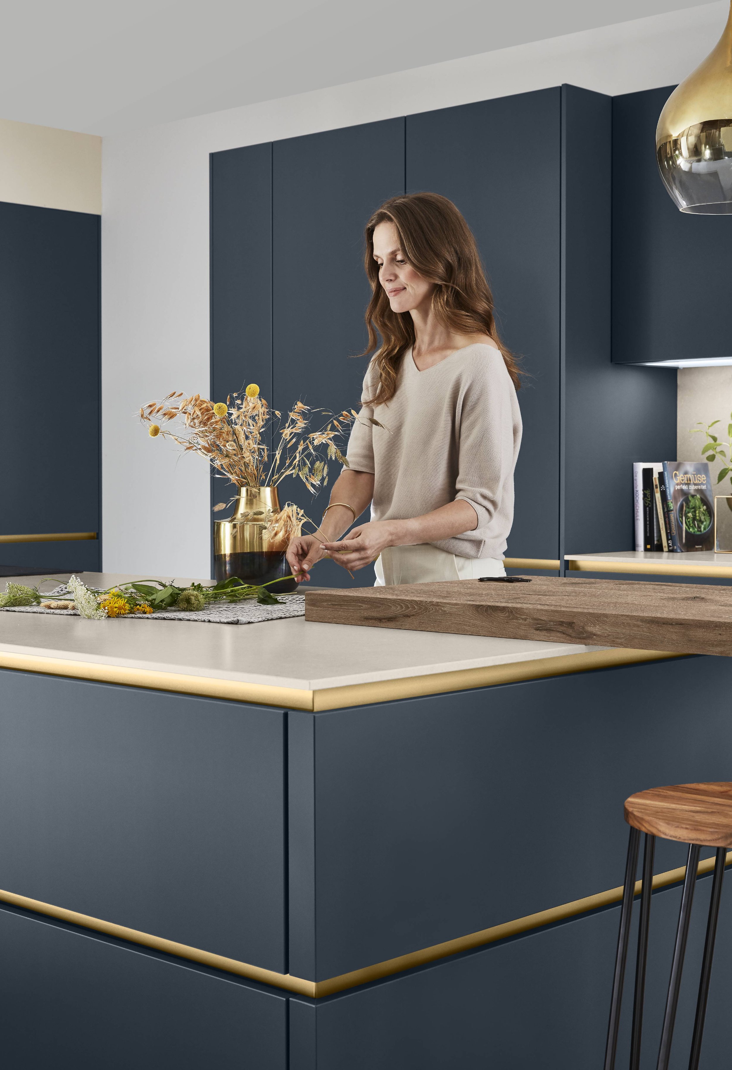 Kvinna arrangerar en bukett med blommor i ett modernt kök med blå skåp och en köksö med vit yta.