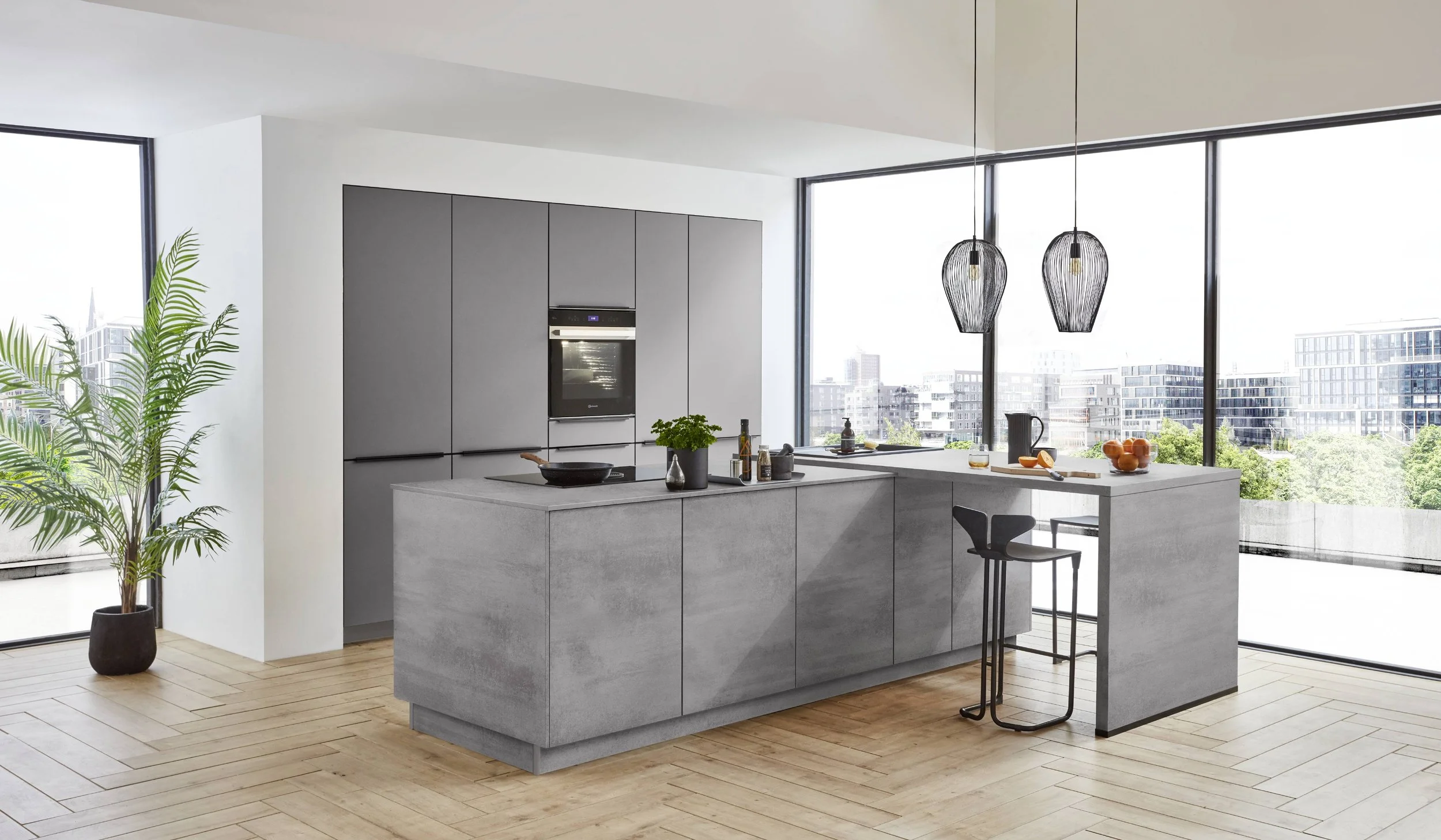 Modern köksinredning med grå skåp, köksö och sittplats, stora fönster som visar stadssilhuett och gröna träd, ljust trägolv, två svarta hänglampor.