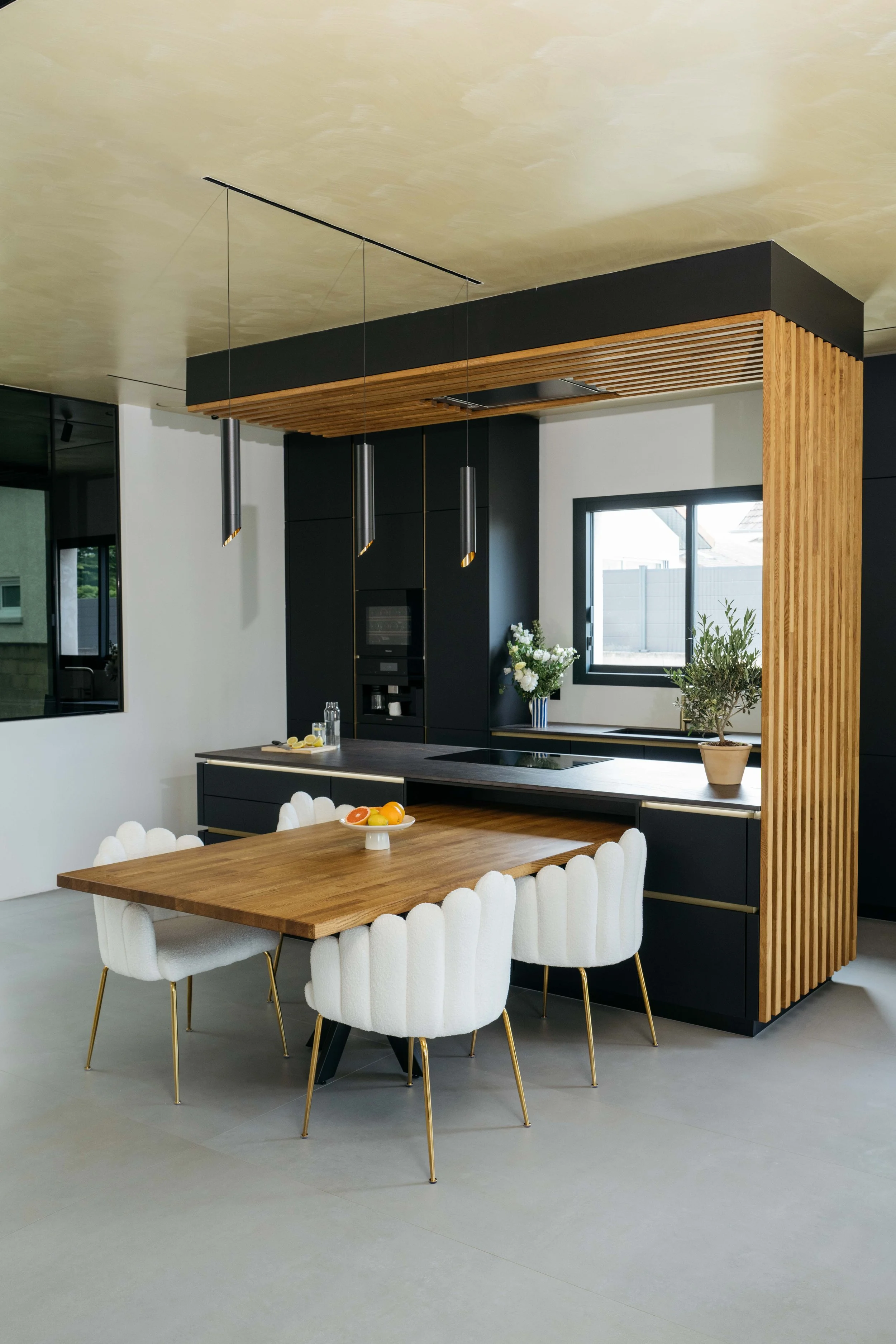 Modernt kök med svart skåp, träbord och vita stolar.