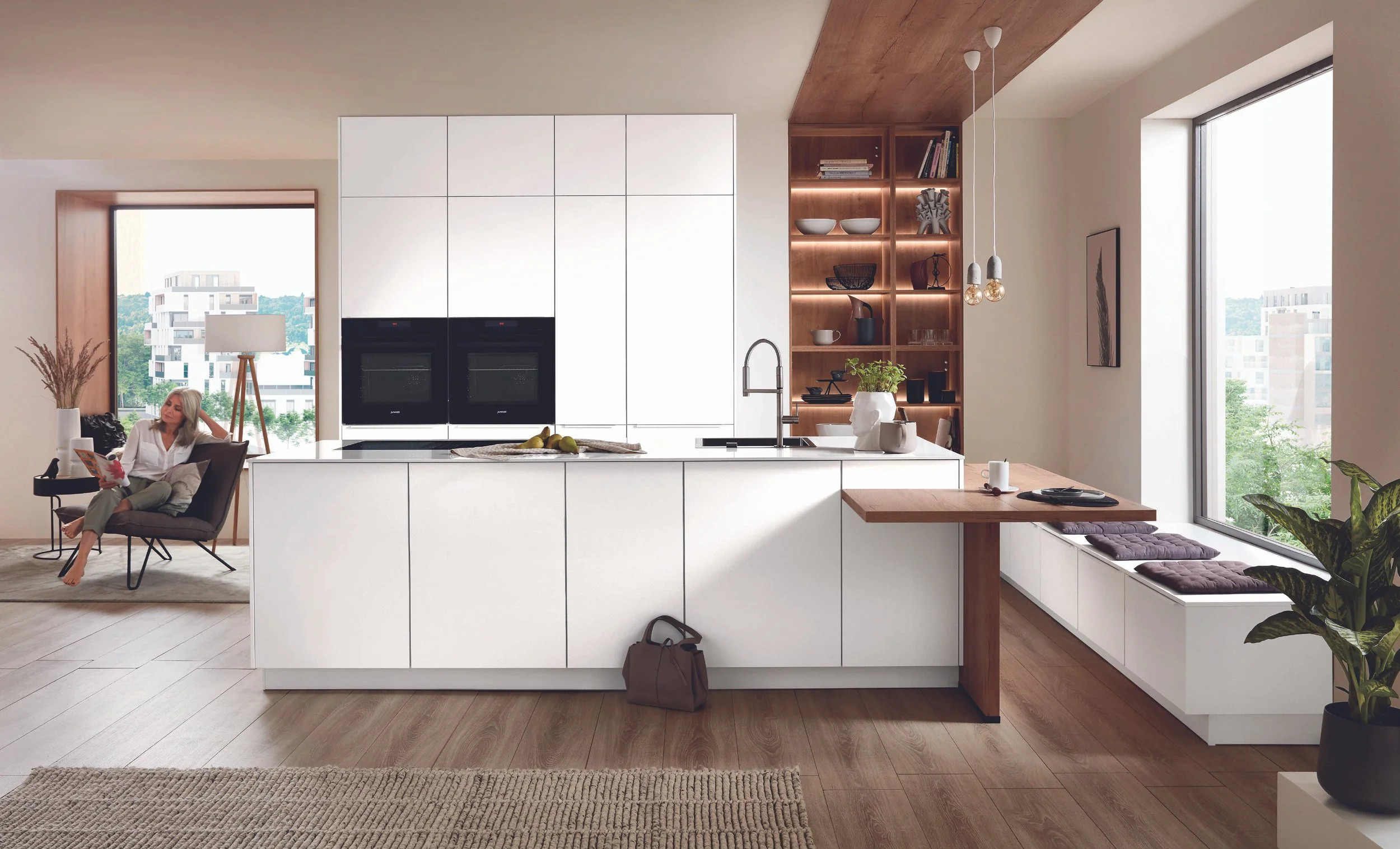 Moderna kök med vita skåp och en köksö, soligt fönster med stadsutsikt, växter och vardagsrum i bakgrunden