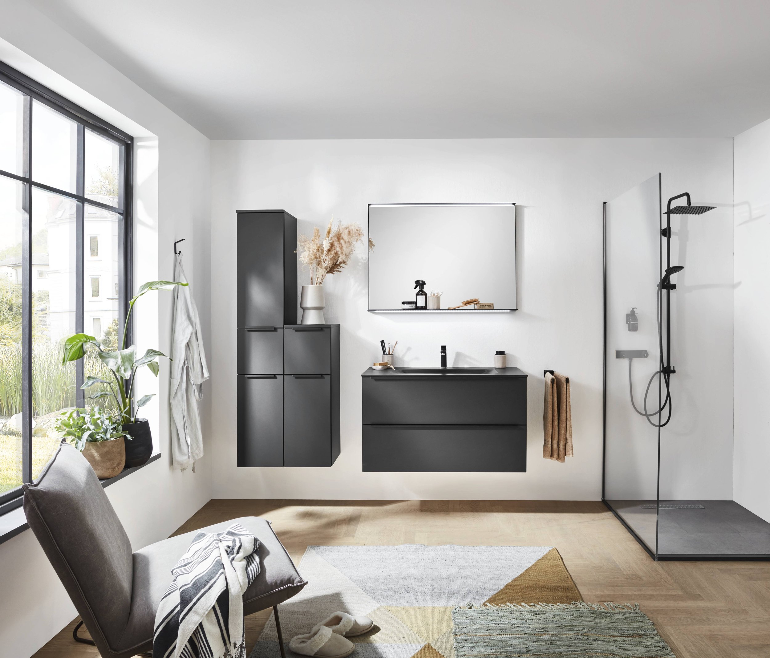 Moderne badrum med svarta skåp, spegel, växt, stolen, litet matta, duschutrymme med svart tak och väggar, fönster och vita väggar.