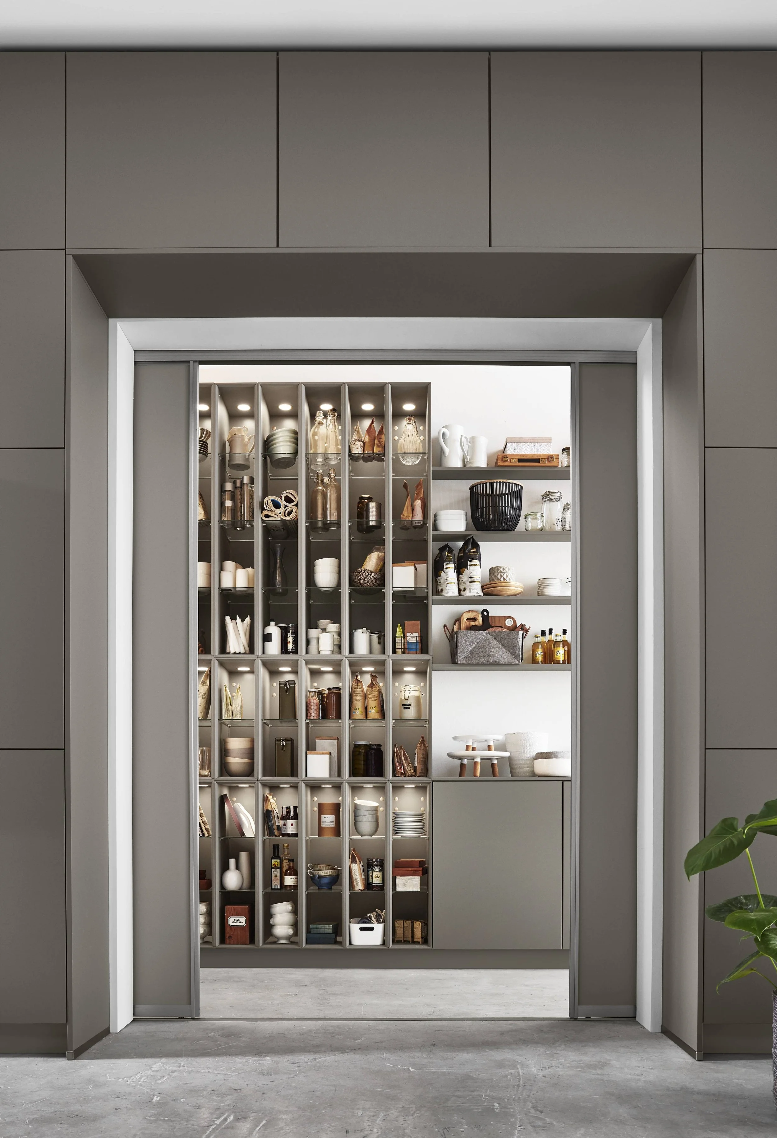 Ett köksskåp fyllt med porslin, glas, kryddor och andra köksartiklar, sett genom en öppning i en vägg.