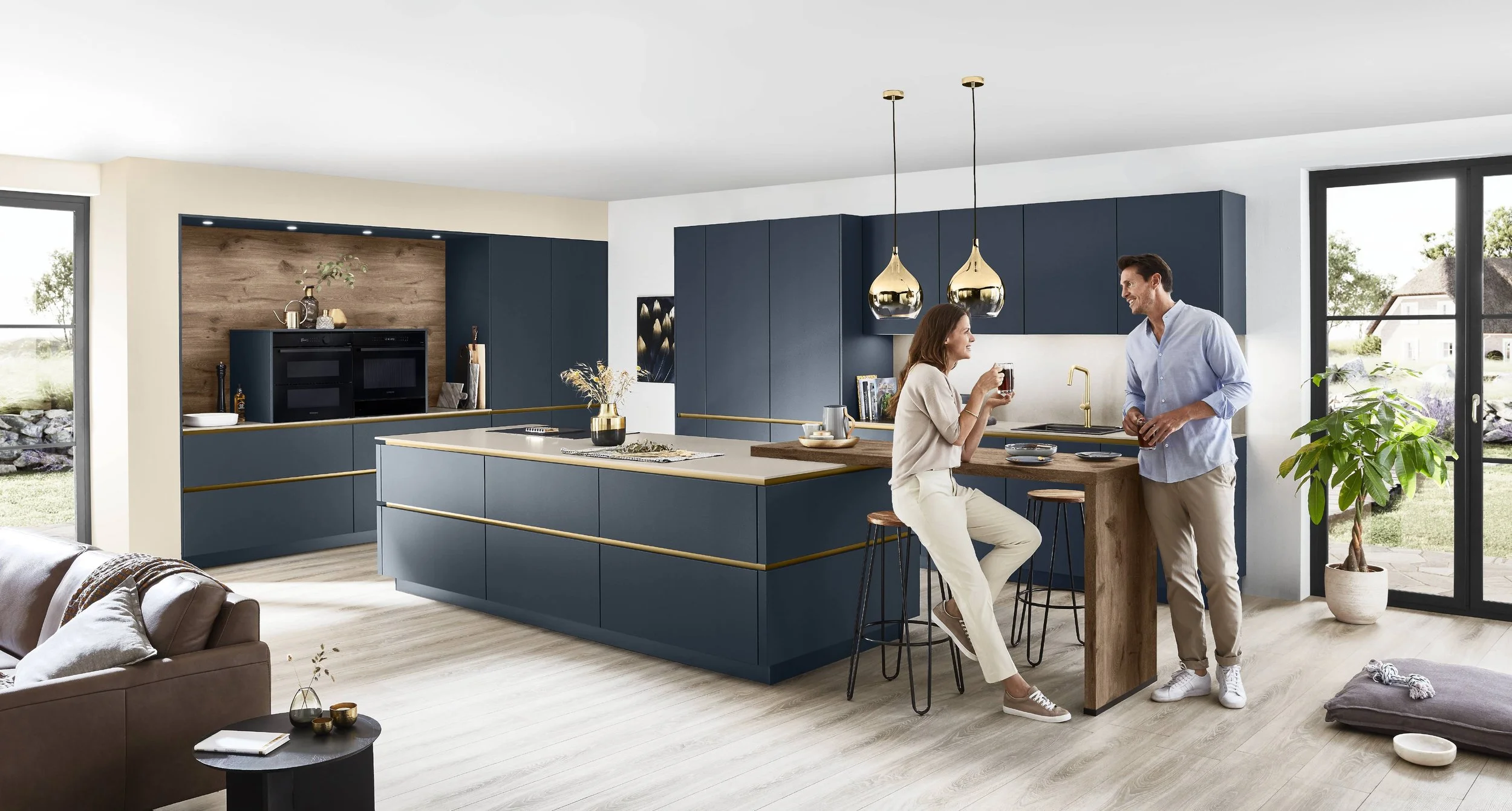 Två människor i ett modernt kök, en kvinna sitter på en köksö och dricker något, en man står och pratar med henne.