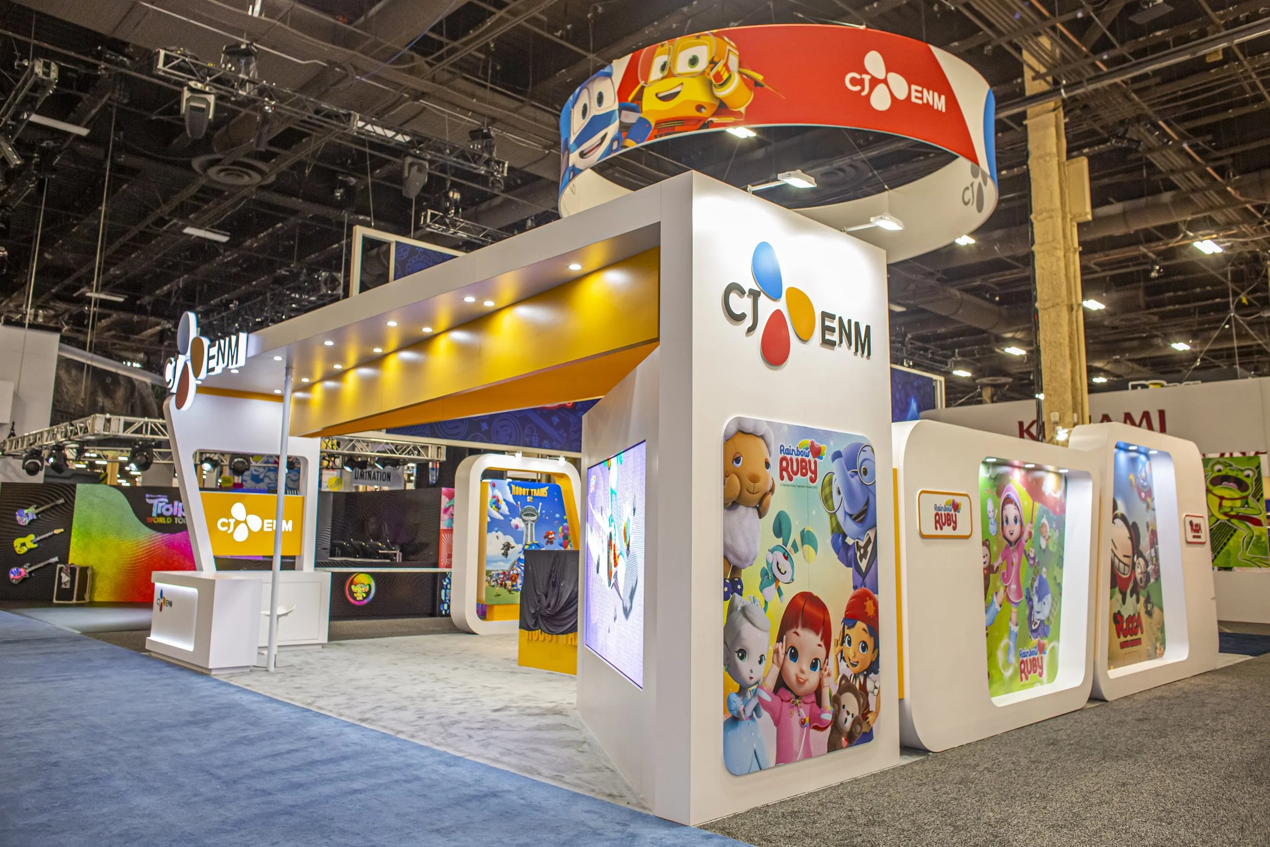 Trade show booth with CTENM branding, featuring advertisements for Rainbow Ruby and other children's shows, illuminated displays, and colorful banners.